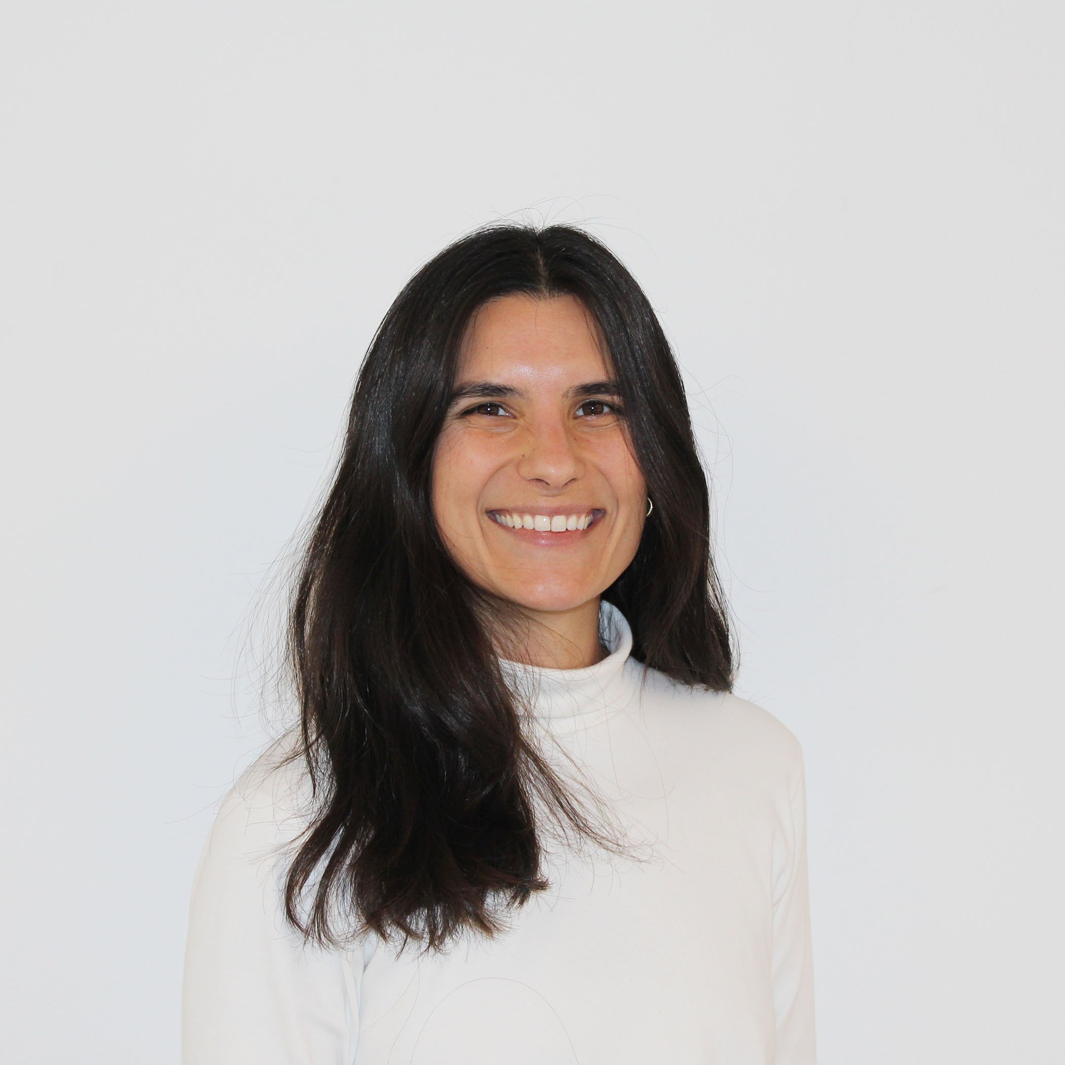 Portrait of a woman with long dark hair wearing a white top, smiling against a plain white background.