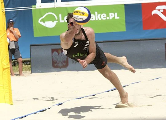Beach volleyball player diving to hit the ball on sand court during a match.