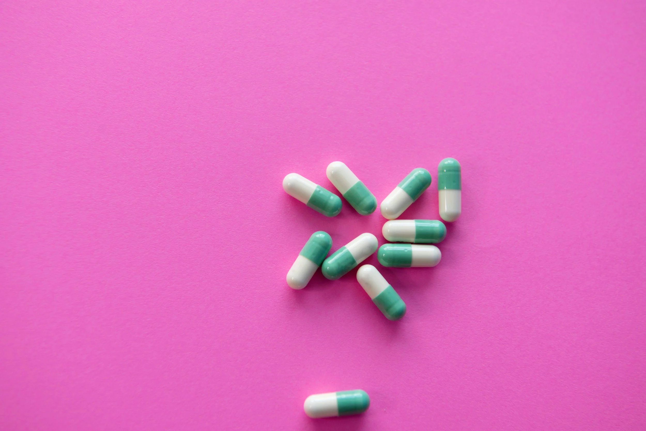Green and white capsules scattered on a pink background.