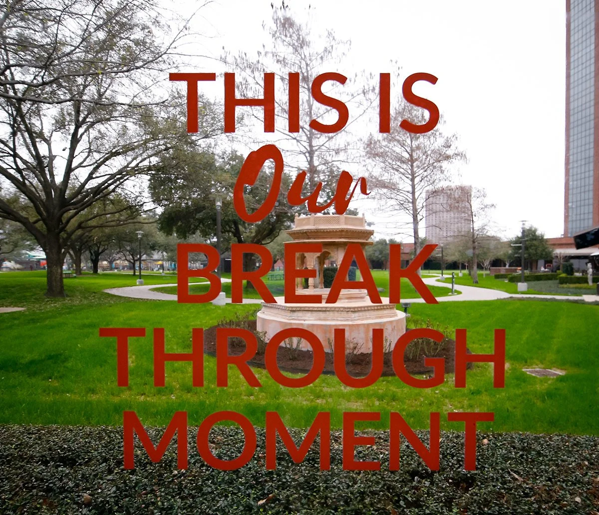 A park with green grass, trees, a fountain, and tall buildings in the background. The text overlay reads 'This is our break through moment' in red letters.