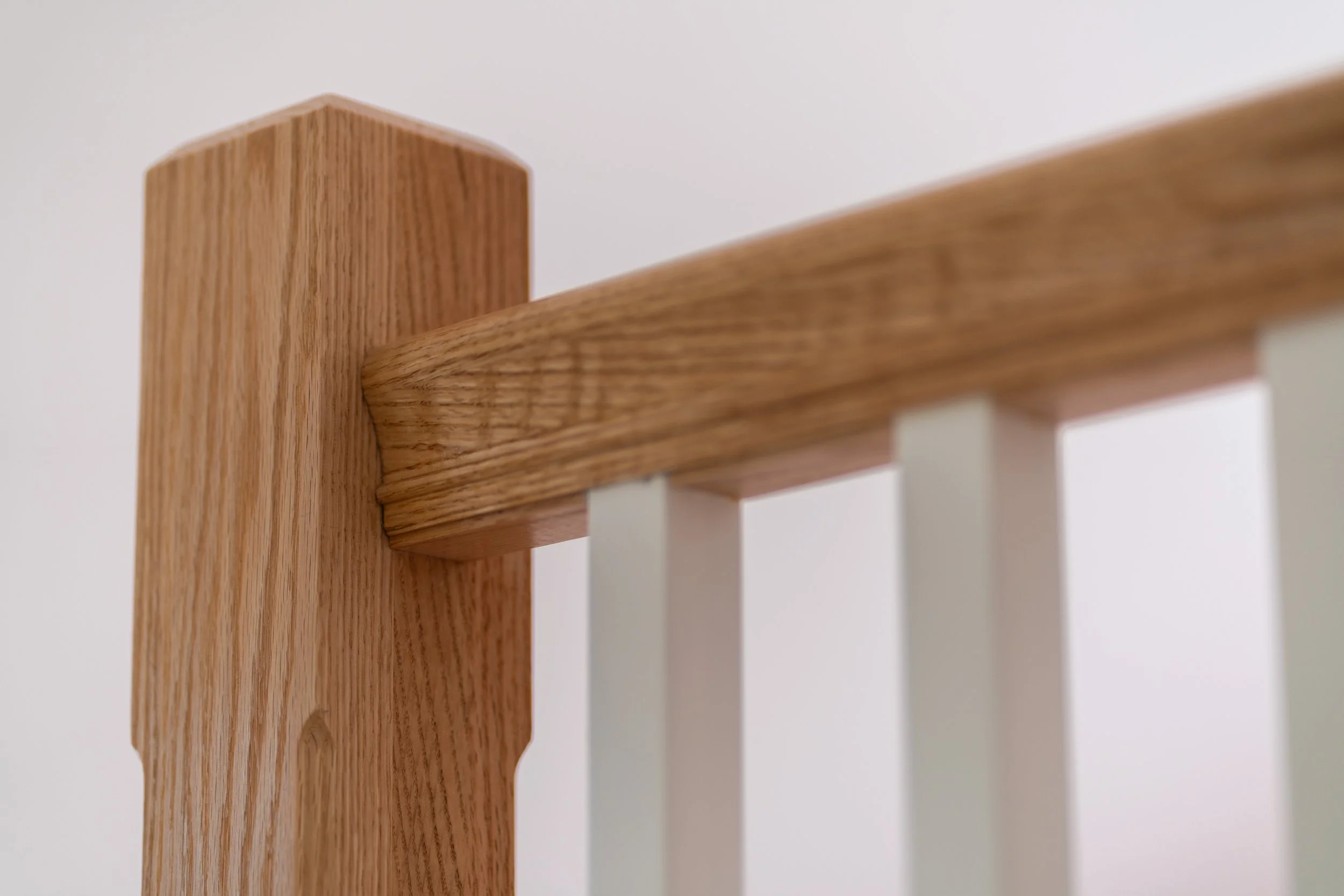 Close-up of a wooden stair railing with a smooth, rounded top, against a plain white wall.
