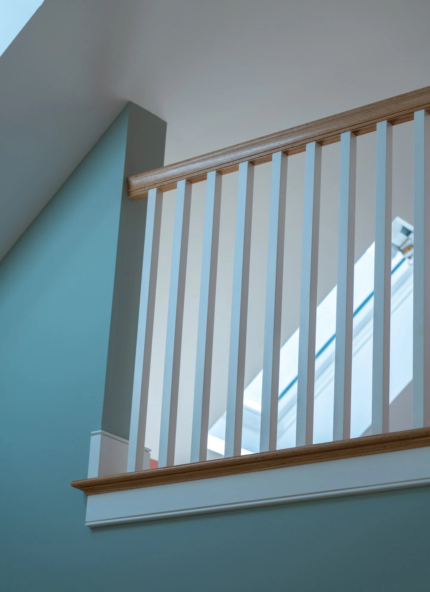 Interior view of a staircase with a wooden handrail and white balusters, against a teal wall and a ceiling with a corner.