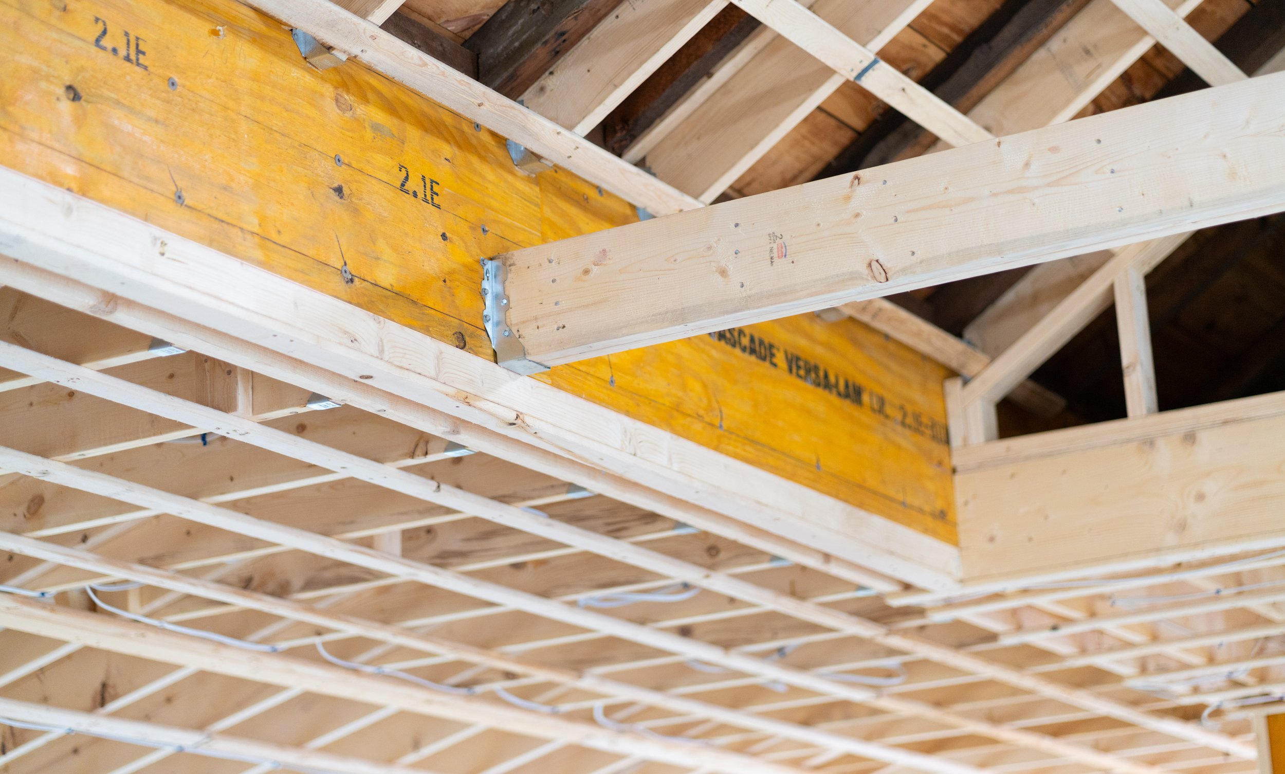 Interior view of a building under construction showing wooden framing, electrical wiring, and a yellow metal beam marked '2.1E' with metal brackets.