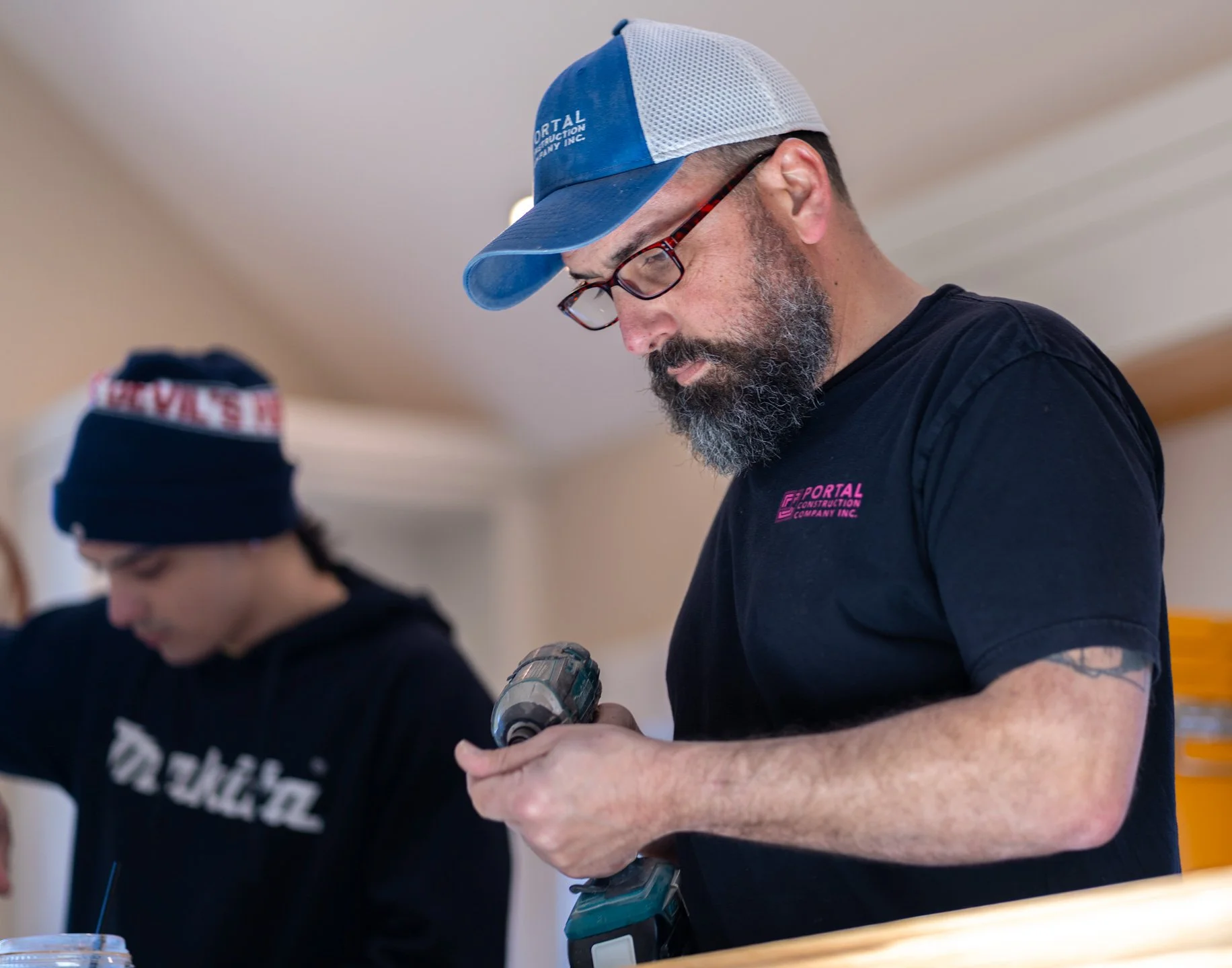 Josh Blakely, Portal Construction owner; wearing glasses and a black Portal Construction shirt, working indoors on a cabinetry project.