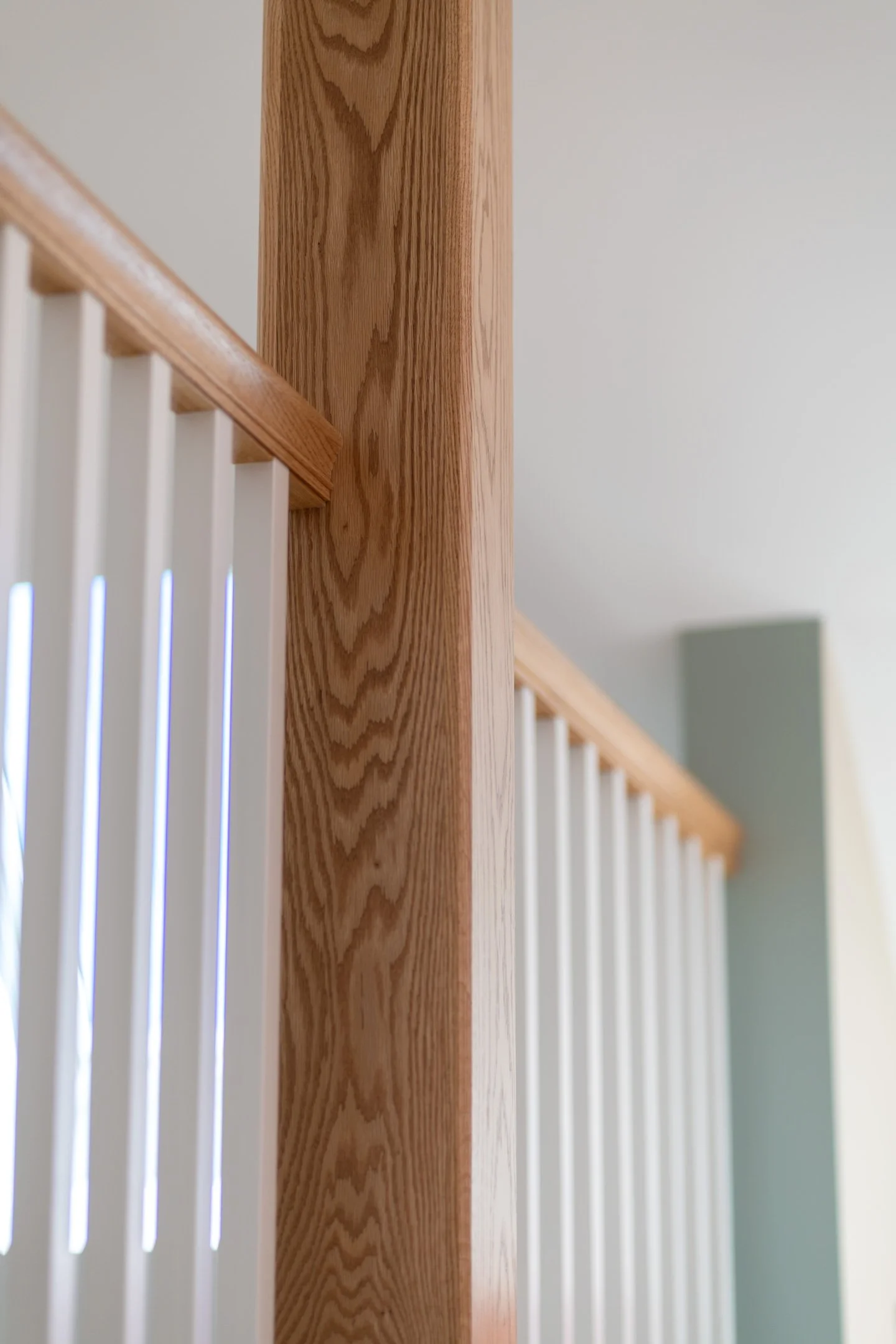 Close-up of a wooden stair railing with white balusters in the background, the photo is taken indoors with neutral wall colors.