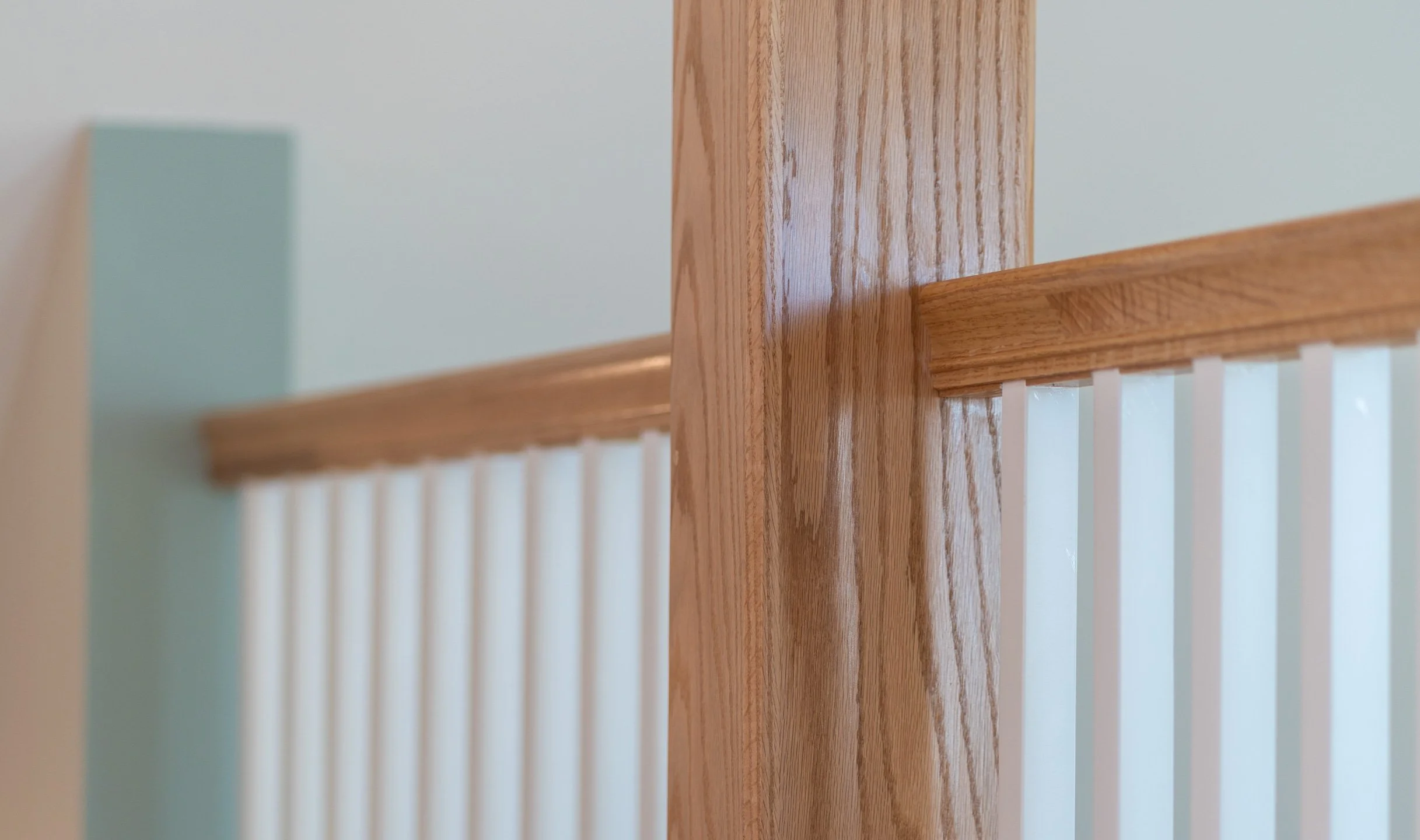 Close-up view of a wooden staircase railing and balusters with a light-colored wall in the background.