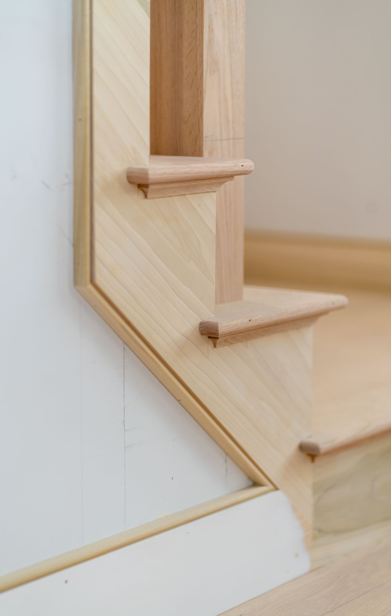 Close-up of a wooden staircase with rounded handrails and a wooden frame, with a plain beige wall in the background.