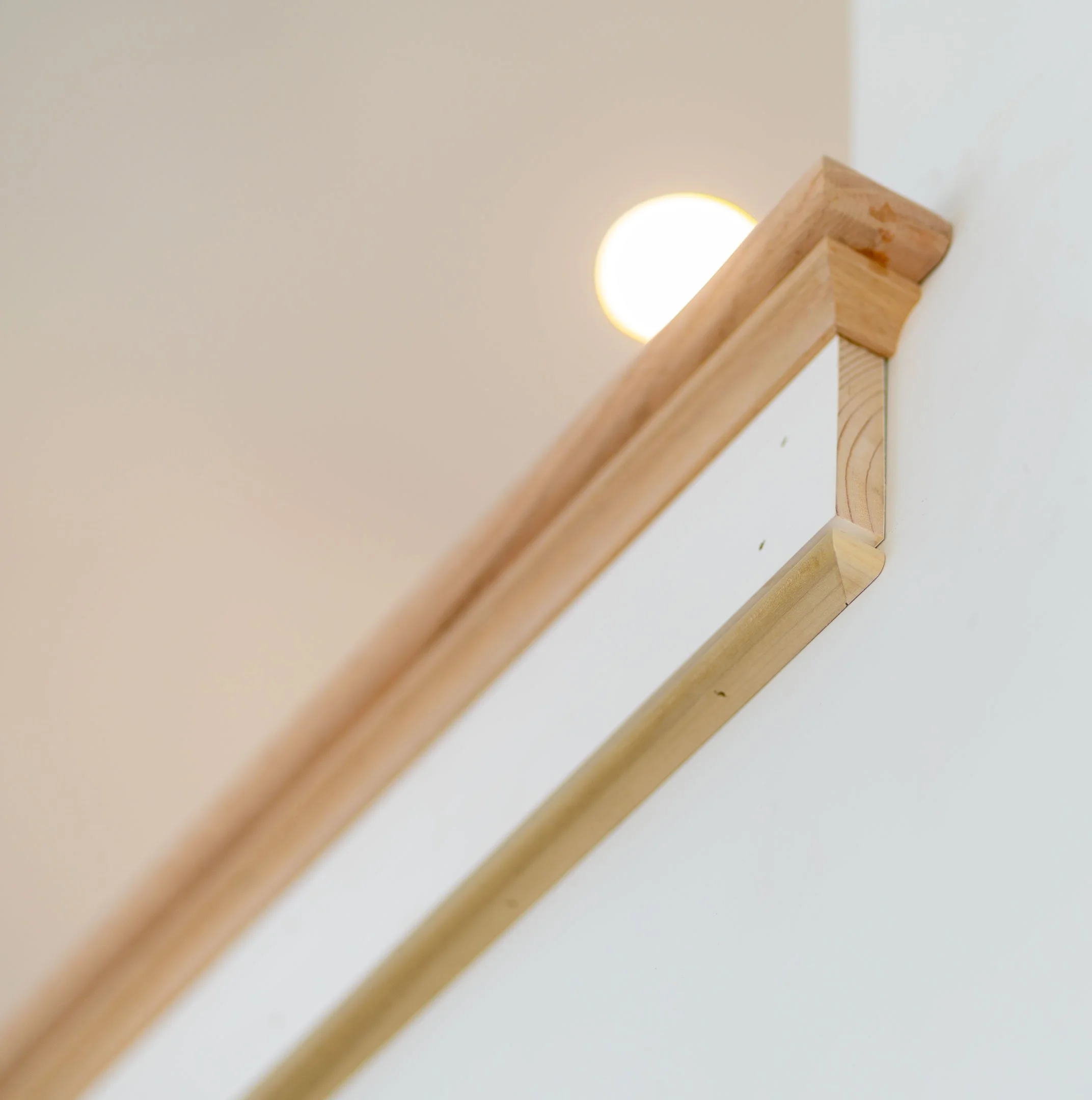 Close-up of a wooden staircase handrail attached to a white wall with rounded corner, illuminated by a nearby light.