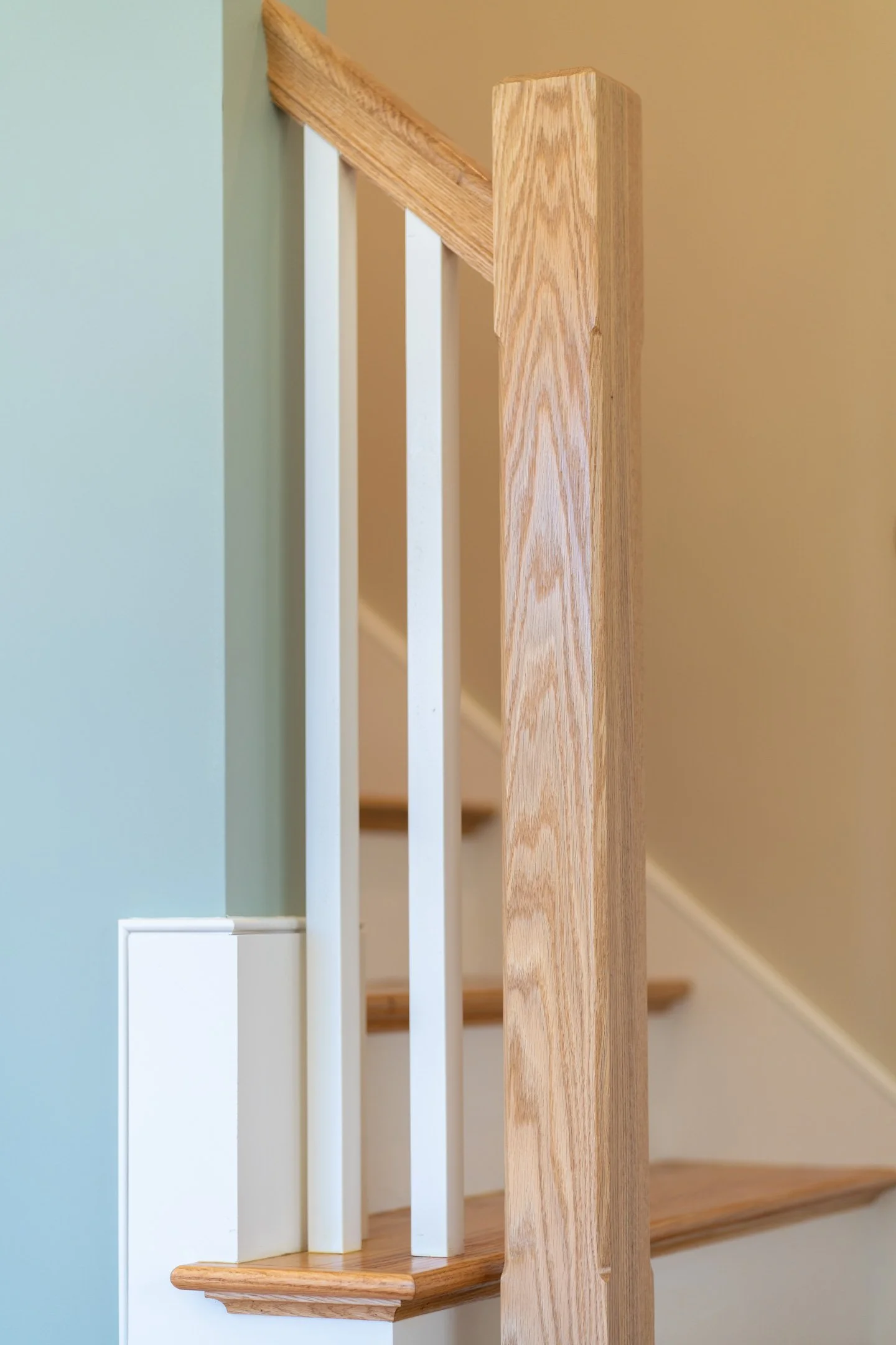 Close-up of a wooden staircase railing with white balusters, wooden handrail, and a wooden newel post.