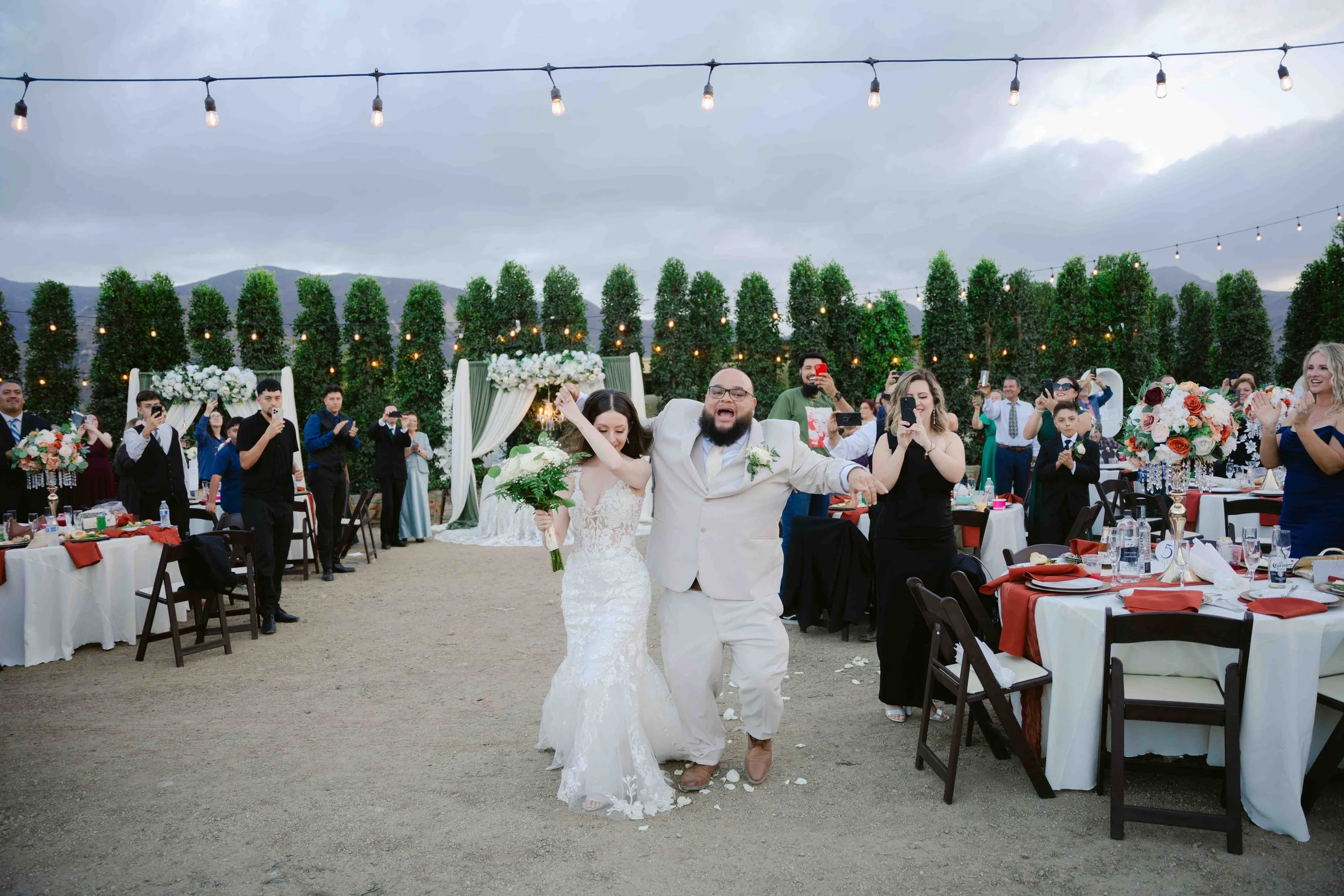 Bride and groom celebrating at their outdoor wedding reception with guests taking photos