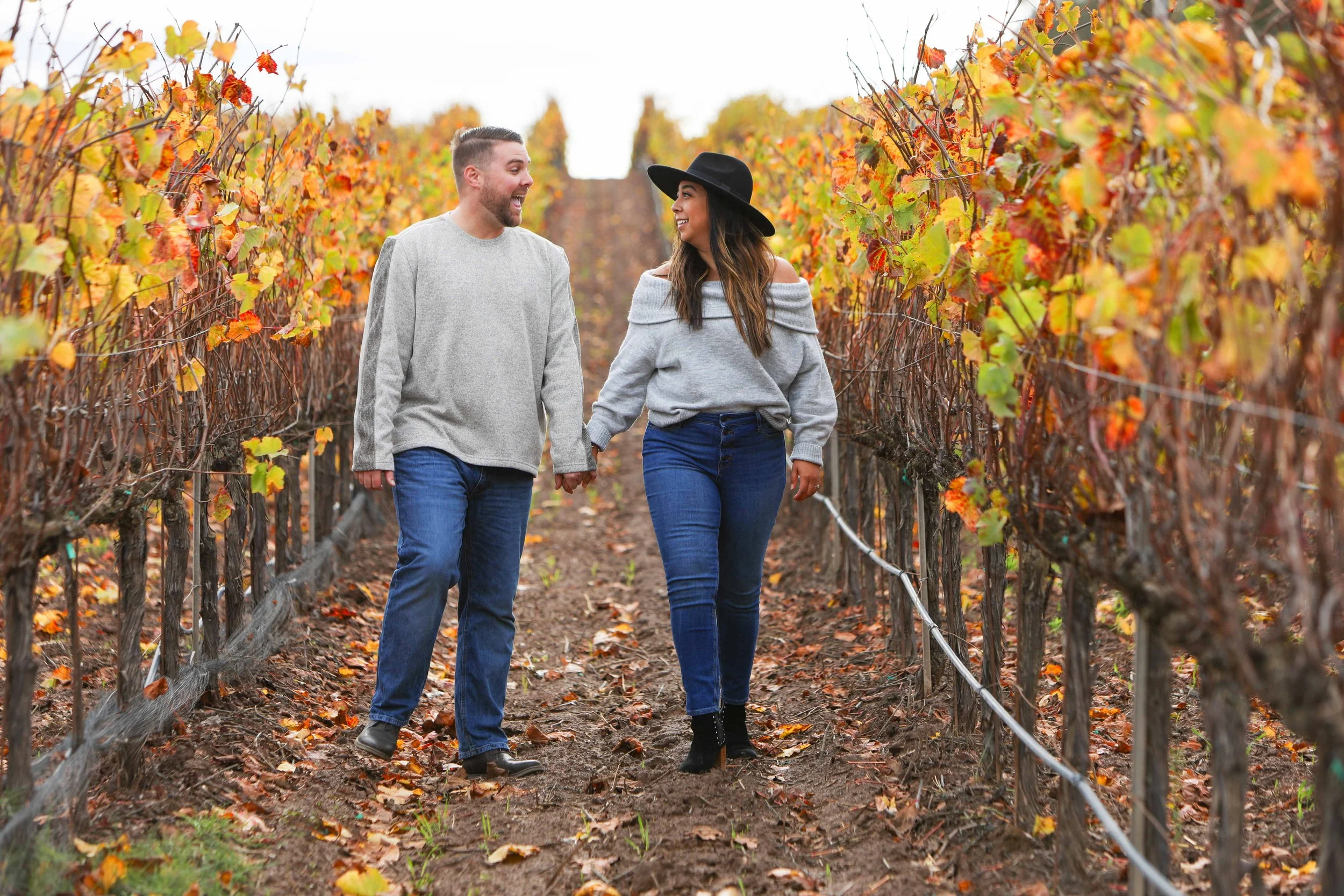 A couple walking hand in hand through a vineyard with colorful autumn leaves.
