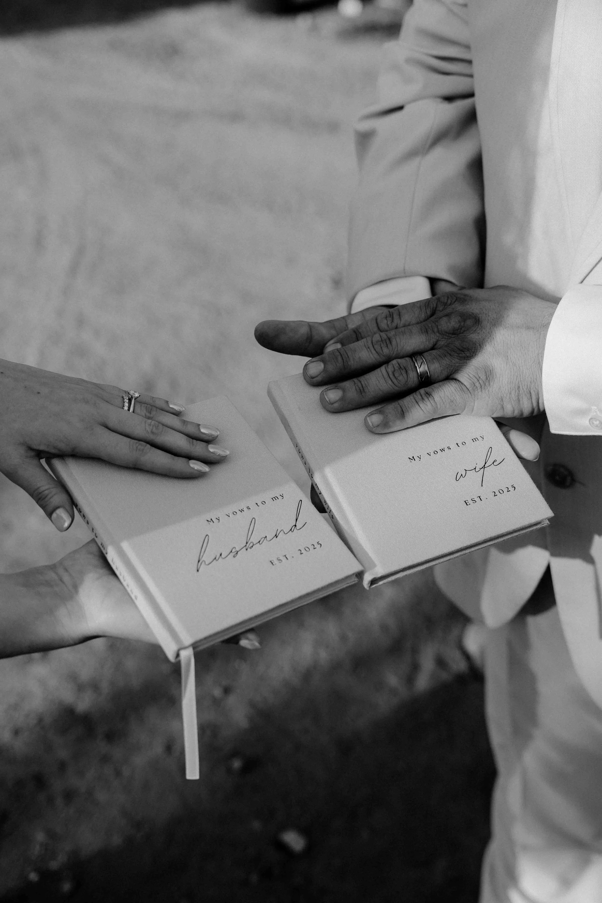 Two people, one man and one woman, holding vow books titled 'My vows to my husband' and 'My vows to my wife,' during a wedding ceremony.