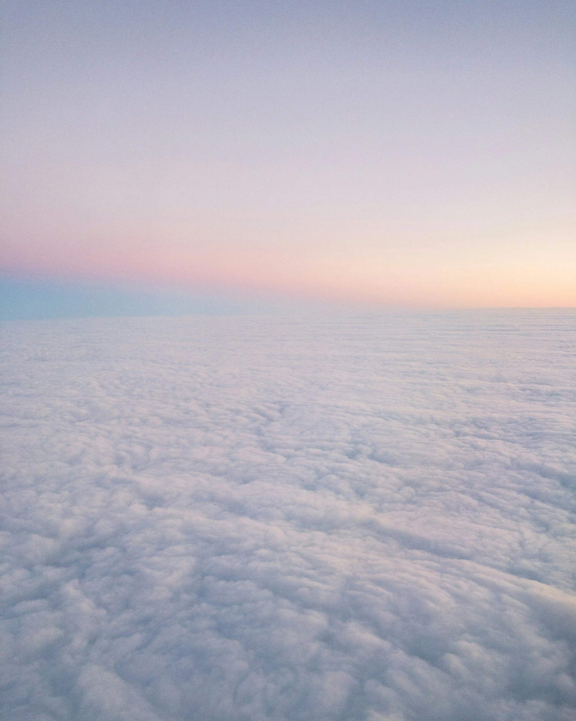 Sky at sunset with pastel pink, purple, and blue hues over a sea of clouds.