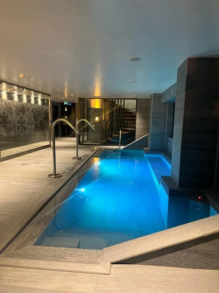 Espace piscine et spa intérieur de L'Hôtel Alpina, avec éclairage bleu et un design moderne. Le lieu est idéal pour la relaxation et le bien-être des participants d'un séminaire Aylo Montagne.