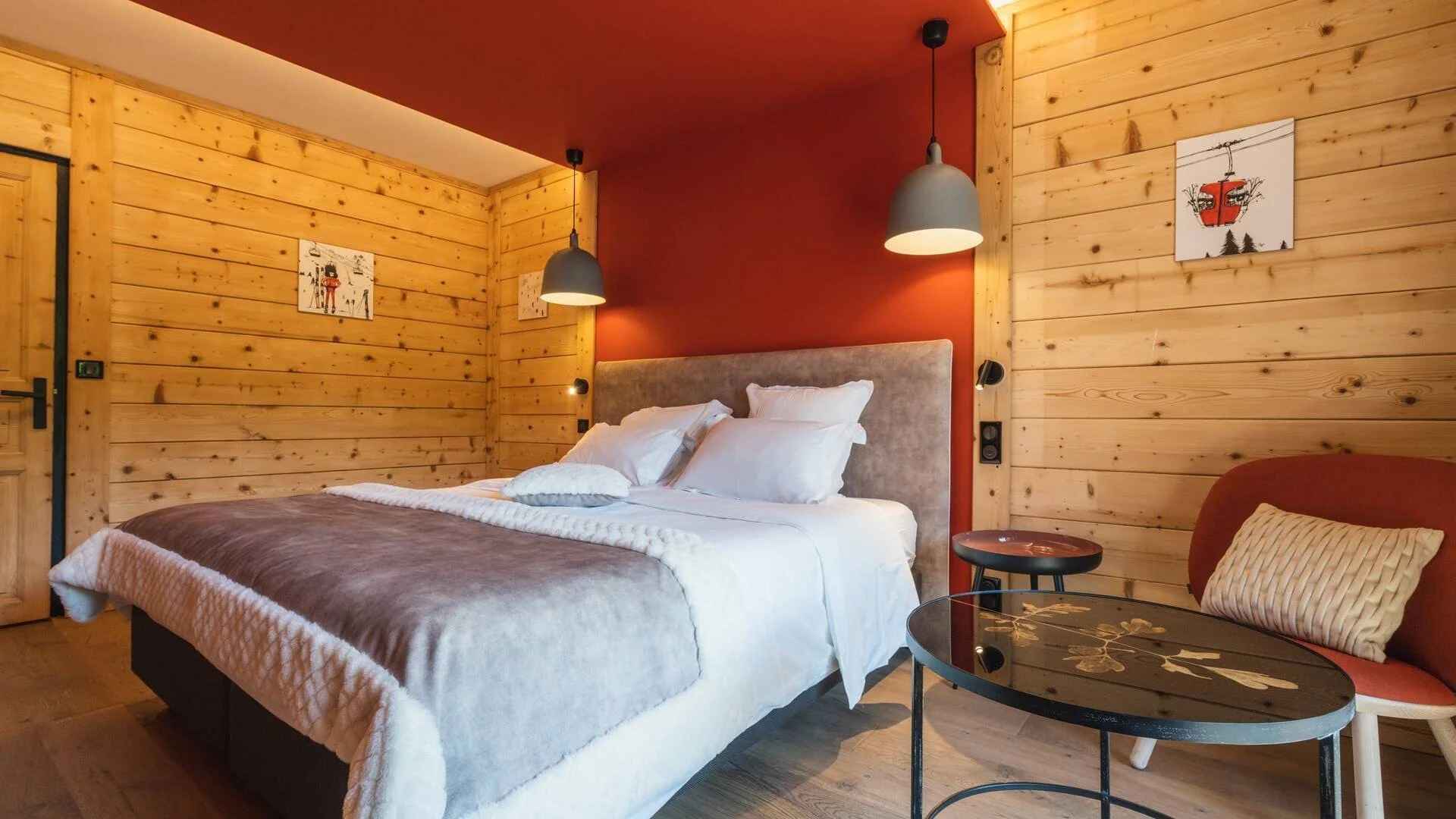 Chambre de style chalet à La Marmotte Hôtel, avec des murs en bois et une palette de couleurs rouge et bois, offrant un espace confortable et intime pour les participants d'un séminaire d'entreprise Aylo Montagne.