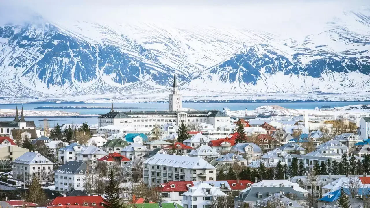 Vue panoramique de Reykjavik, Islande, enneigée en hiver, avec le bâtiment principal de la ville et des maisons colorées sous d’imposantes montagnes enneigées. Un cadre unique pour un séminaire Aylo Montagne.
