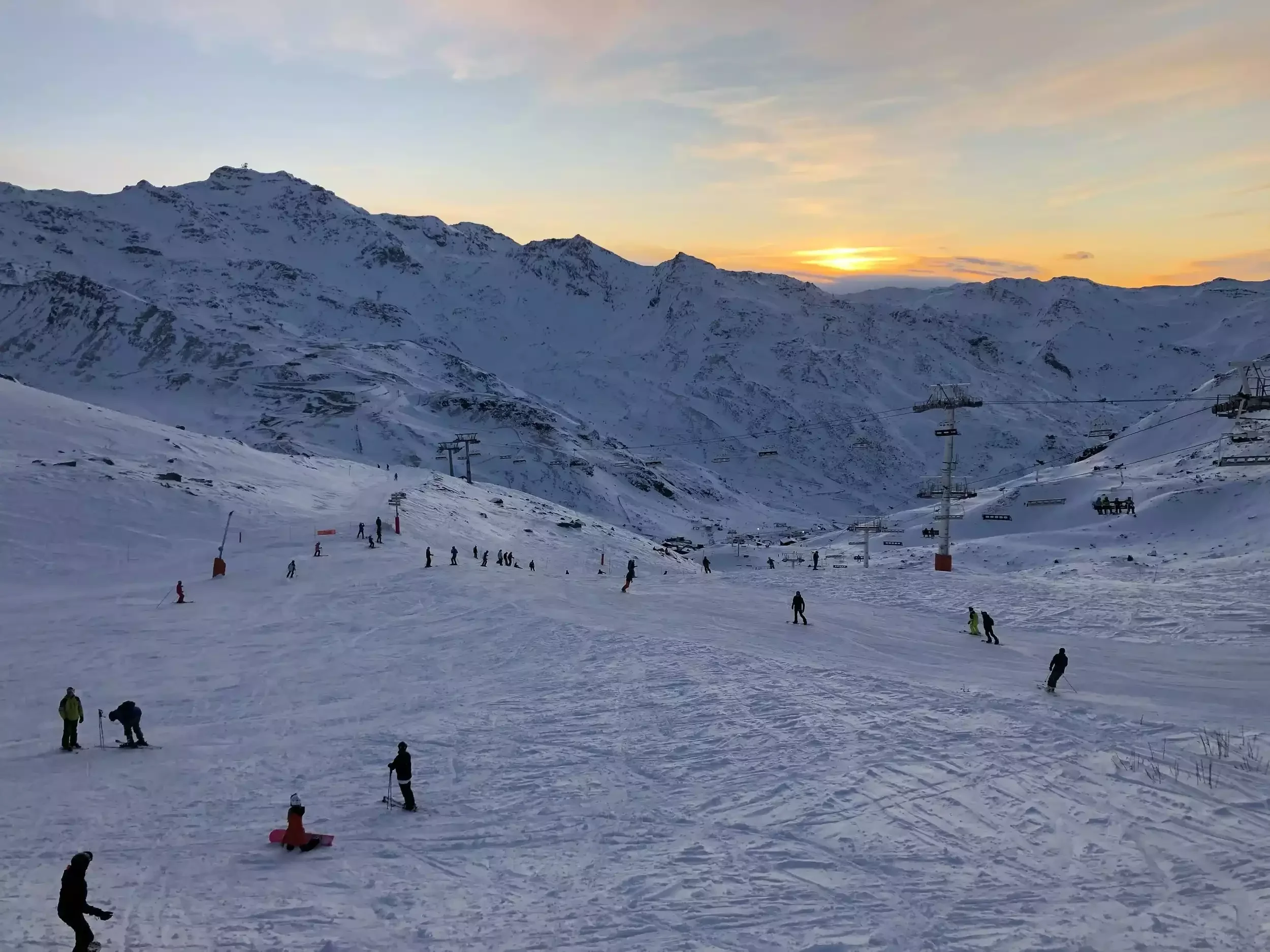Pistes de ski de Val Thorens au coucher du soleil, avec de nombreux skieurs et snowboarders. L'image capture l'atmosphère unique de la fin de journée en montagne, idéale pour un séminaire d'entreprise Aylo Montagne.