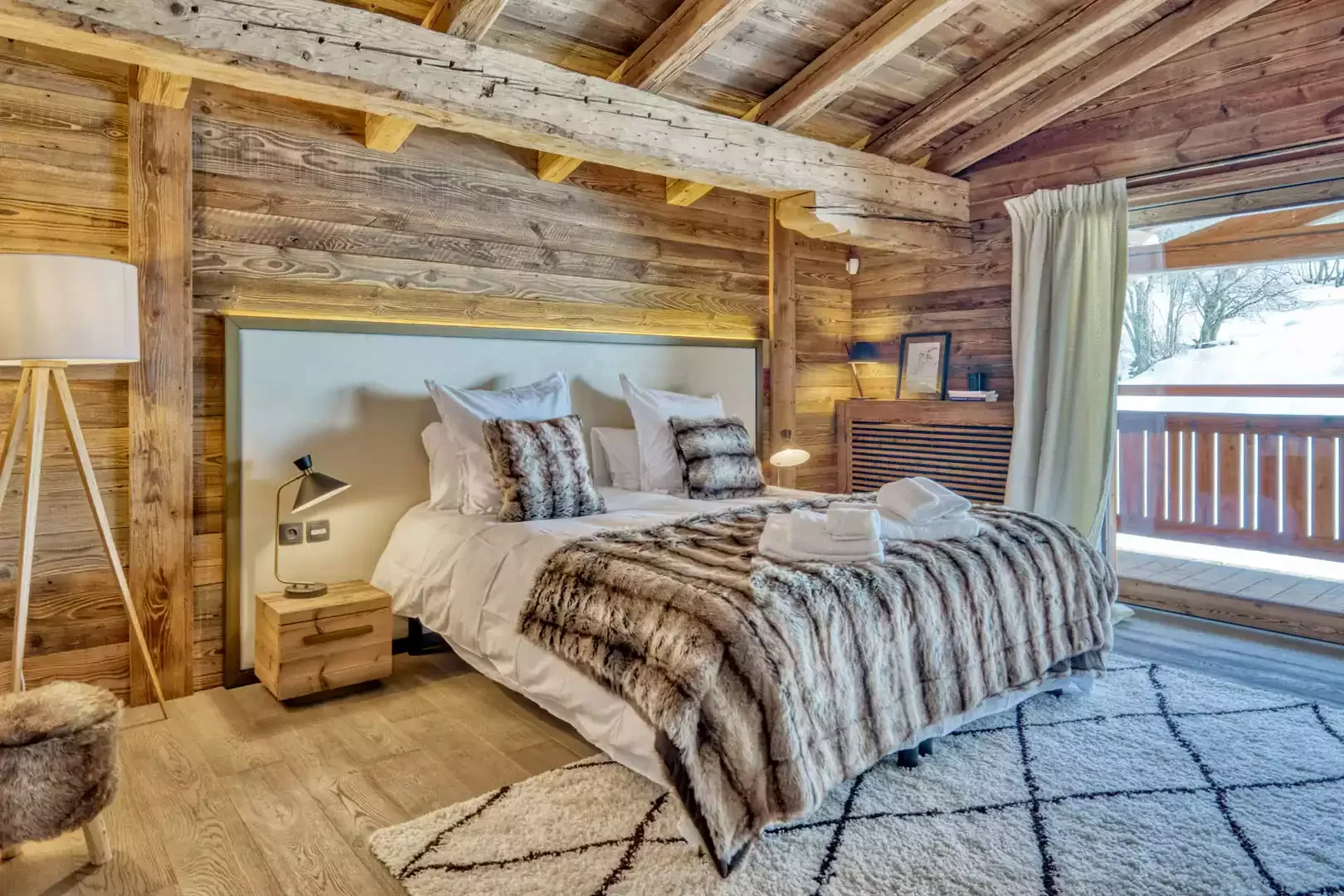 Luxury hotel room at the Hôtel Les Loges Blanches, with wooden walls, cozy king-size bed and faux fur textiles. Optimal comfort for participants in an Aylo Montagne seminar in Megève.