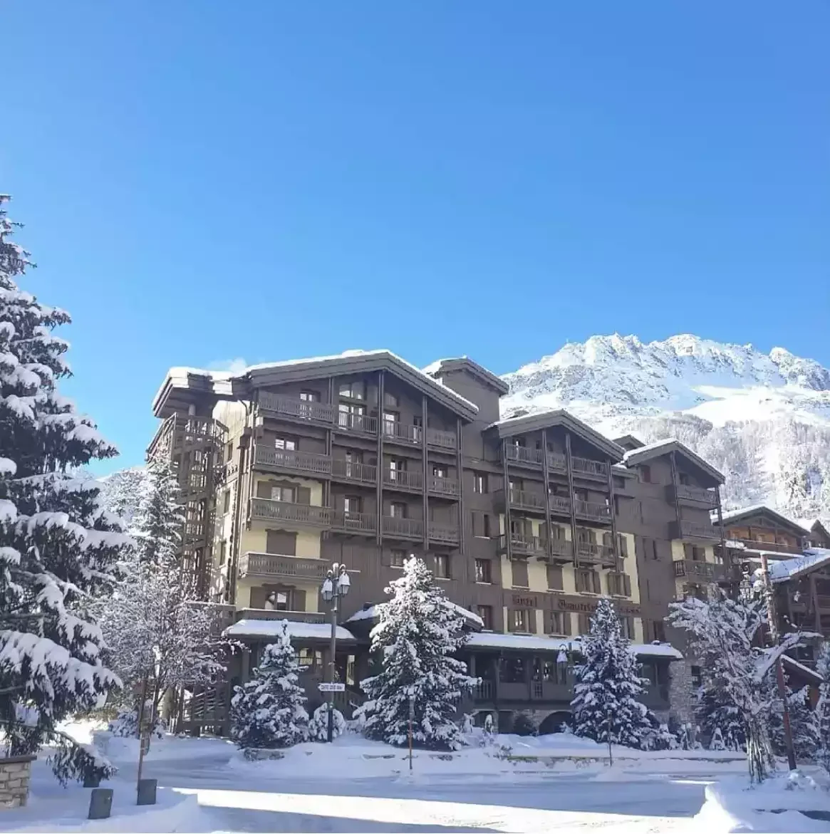 Exterior facade of the Hotel Tsanteleina, a luxurious traditional-style chalet with wooden balconies. The hotel is set in a snowy winter landscape, with a majestic mountain in the background.
