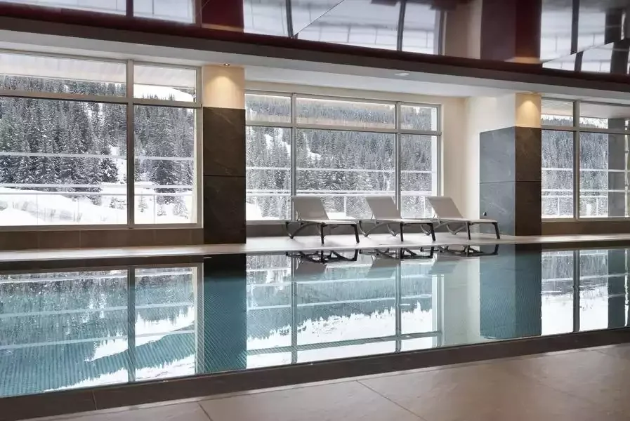 Piscine intérieure chauffée à l’hôtel Alhena & spa, avec de grandes baies vitrées offrant une vue sur le paysage enneigé. C’est un espace idéal pour se détendre après une journée de ski.