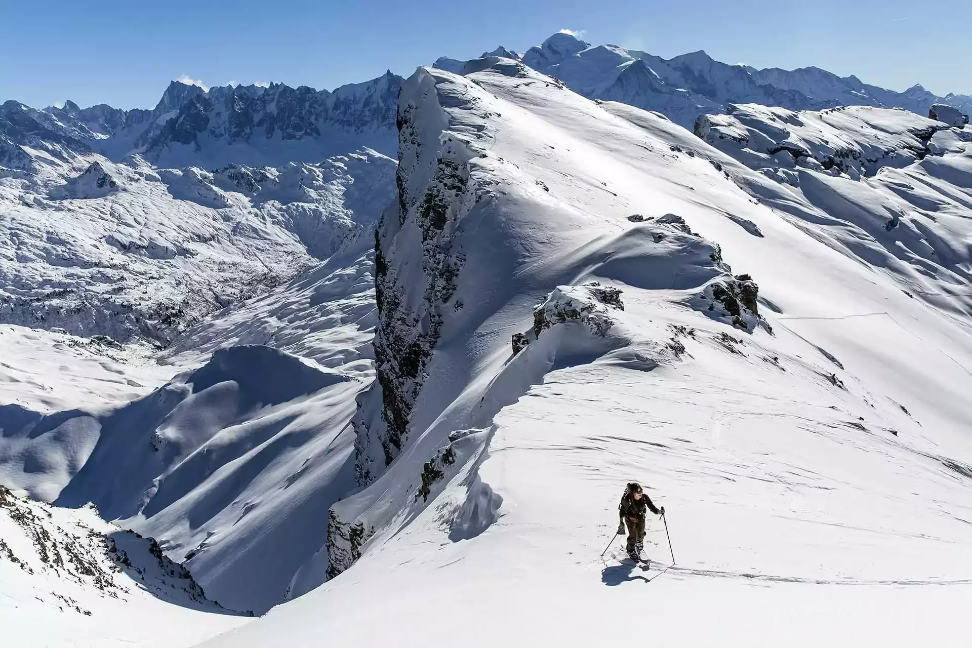 Un participant à un séminaire d’Aylo Montagne pratique le ski de randonnée sur une crête montagneuse à la station de Flaine. Le paysage alpin enneigé est majestueux et spectaculaire, avec des sommets imposants au loin.