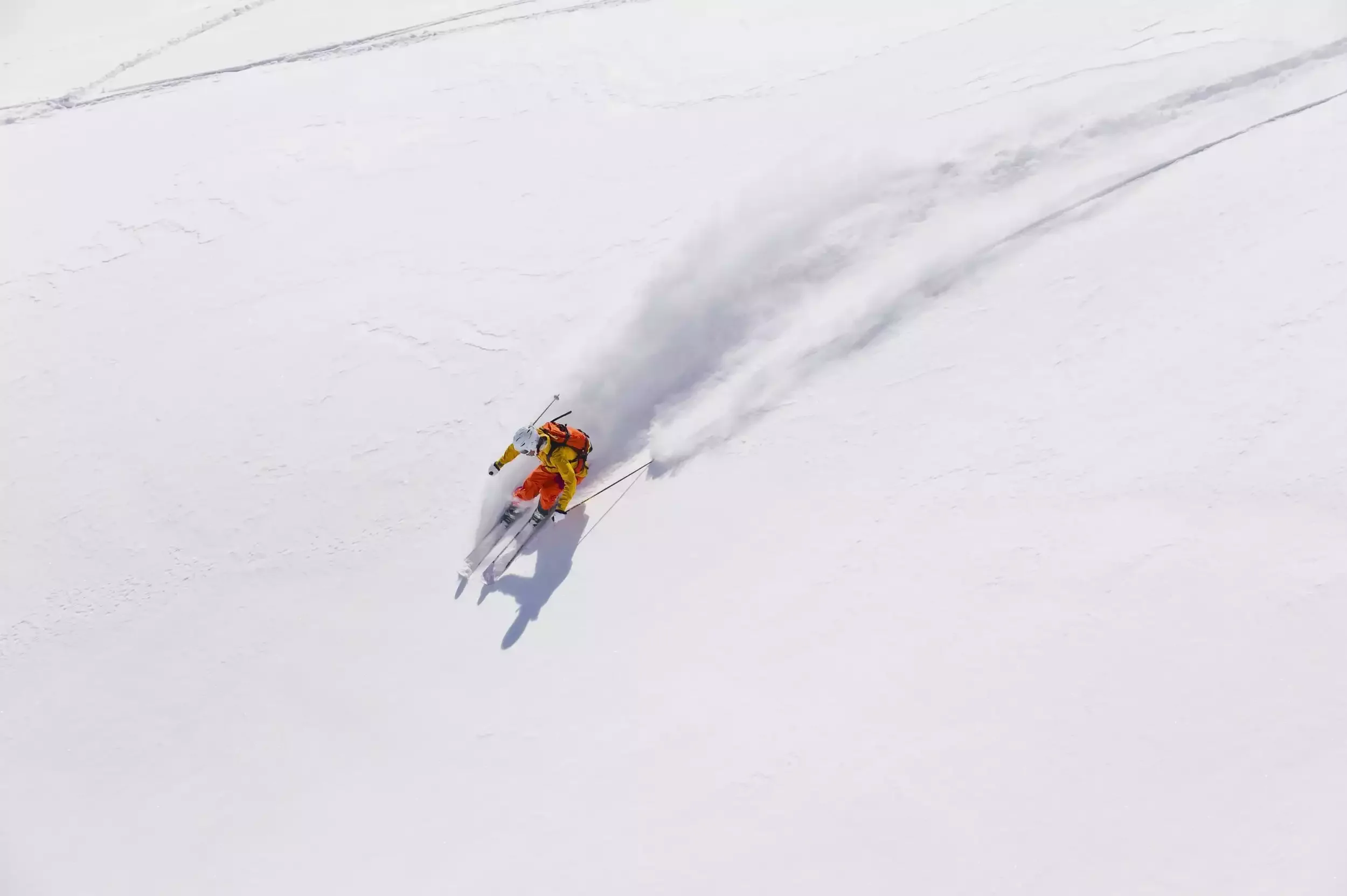 Skieur en veste rouge et jaune descendant à toute vitesse une pente de neige vierge. L’image représente l’aventure et l’adrénaline d’un séminaire Aylo Montagne.