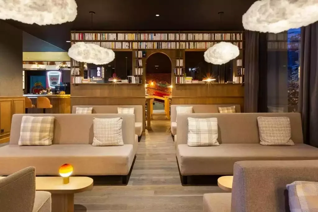 Le hall de l’hôtel Rocky Pop avec des canapés au design moderne, des étagères pleines de livres et un éclairage chaleureux qui crée une atmosphère accueillante et idéale pour la socialisation des clients.