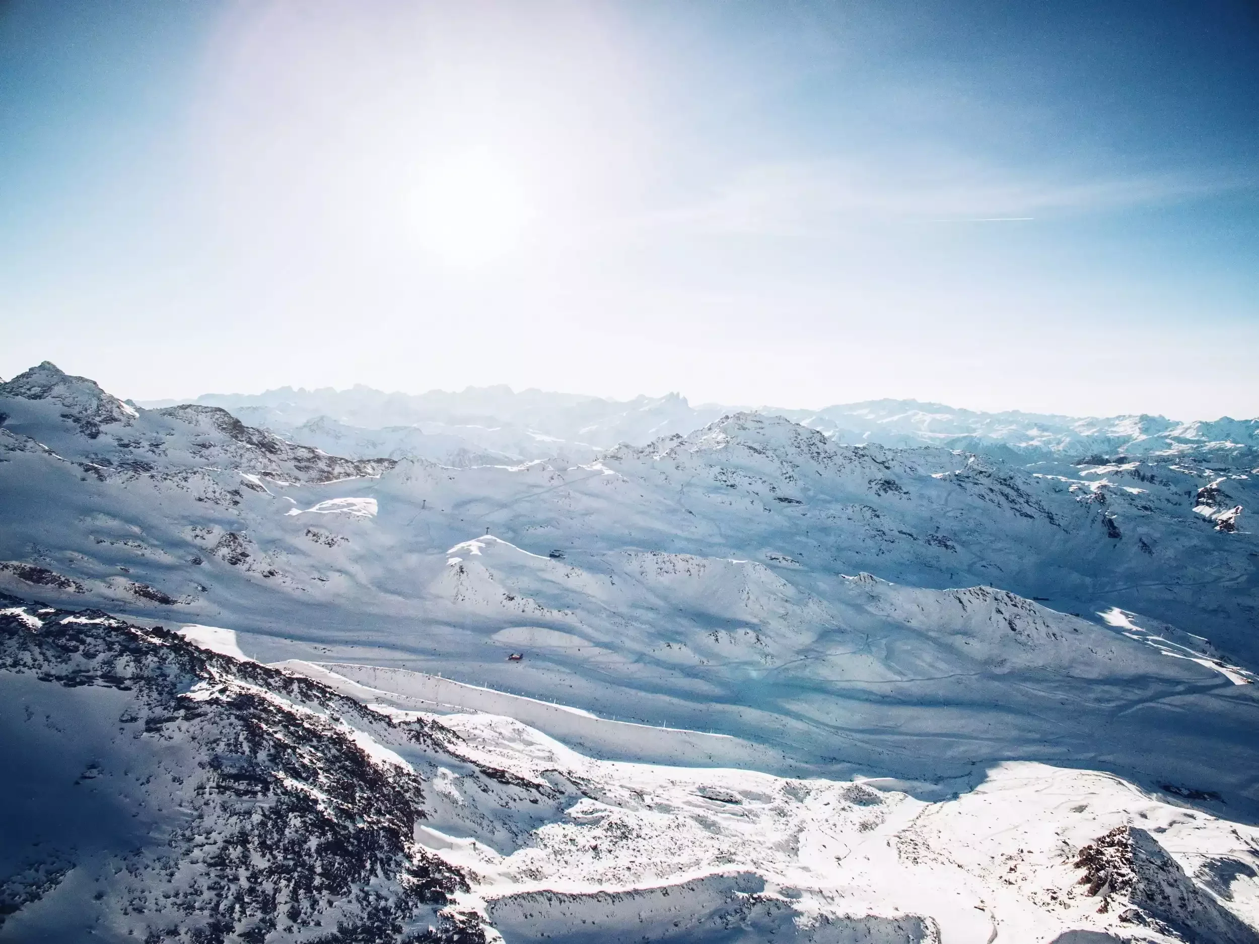 Panoramic view of the snow-covered slopes of Les Menuires. The photo, in bright light, shows ski slopes descending between rocky peaks, with chairlifts in the distance.