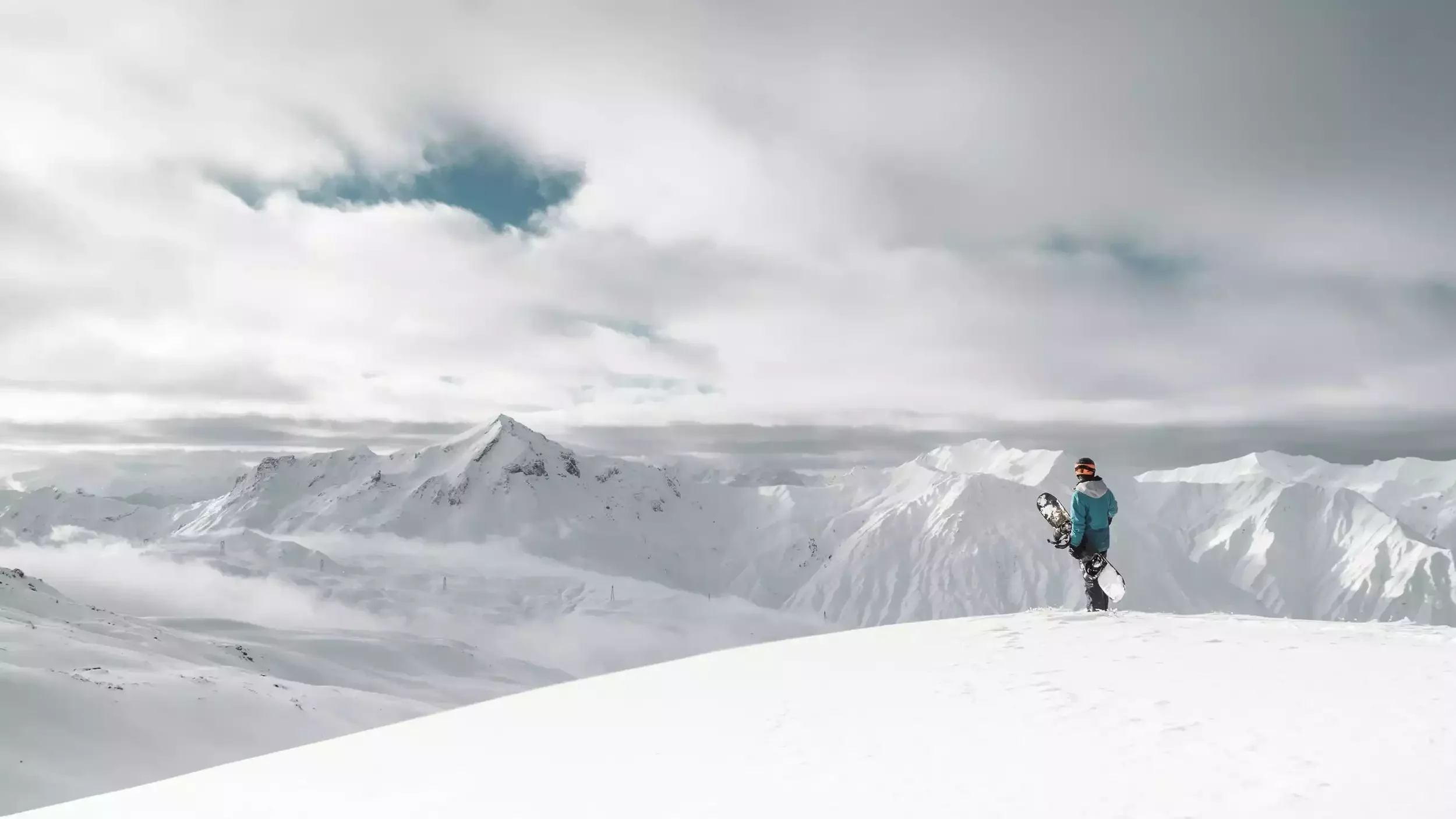 A snowboarder at the top of a mountain in Les Menuires stops to admire the majestic landscape of snow-capped peaks and slopes.