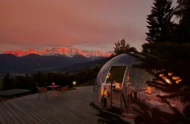 Geodome de luxe sur la terrasse d’un chalet dans les Alpes, avec un dîner intime et vue sur les montagnes illuminées par le coucher du soleil, lors d’un séminaire avec Aylo Montagne