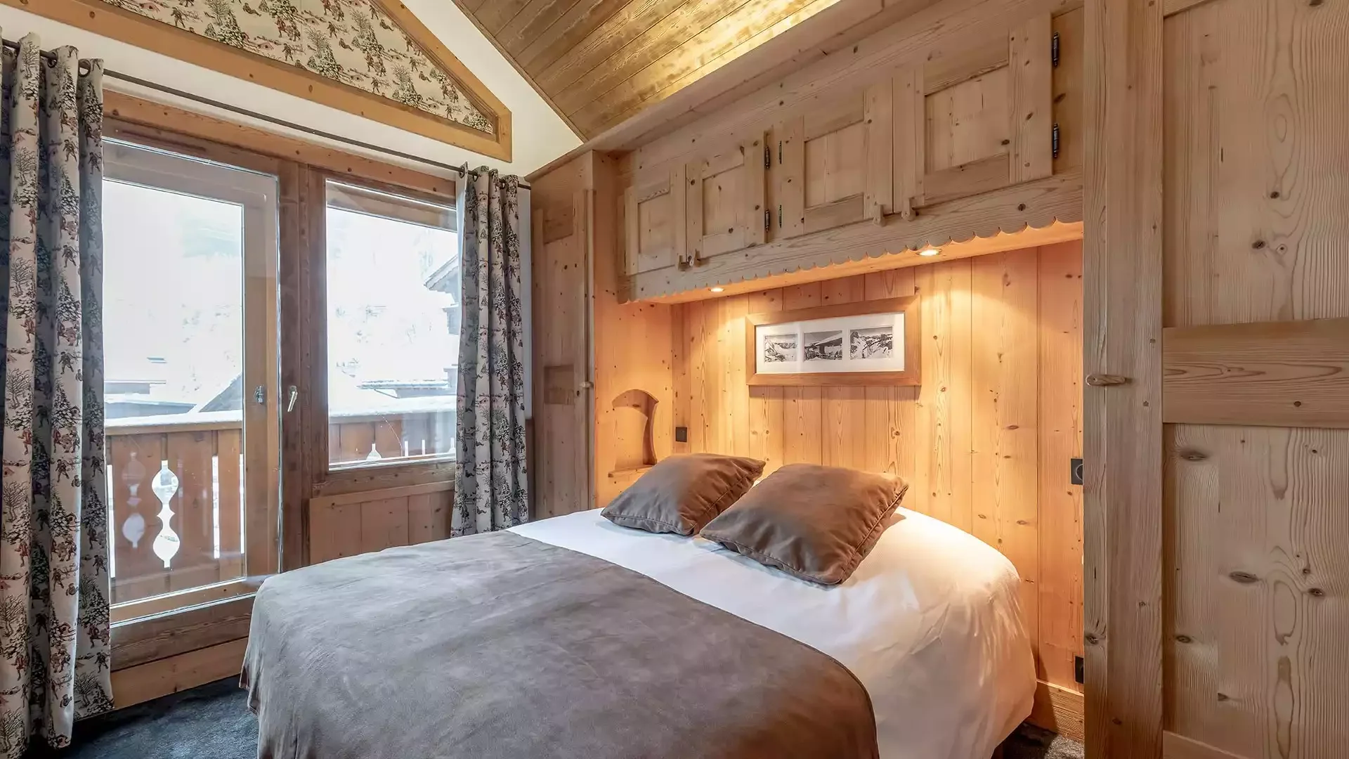 Hotel room with rustic wooden decor at Hôtel L'Eternlou. The space features a queen-size bed and a balcony that opens onto the mountain, creating a welcoming atmosphere.