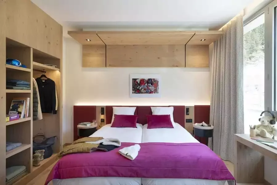 Chambre design à l’Alhena & spa hôtel avec un grand lit, tête de lit magenta, et les murs en bois clair. L’espace, avec son décor élégant et fonctionnel, est conçu pour le confort des clients.