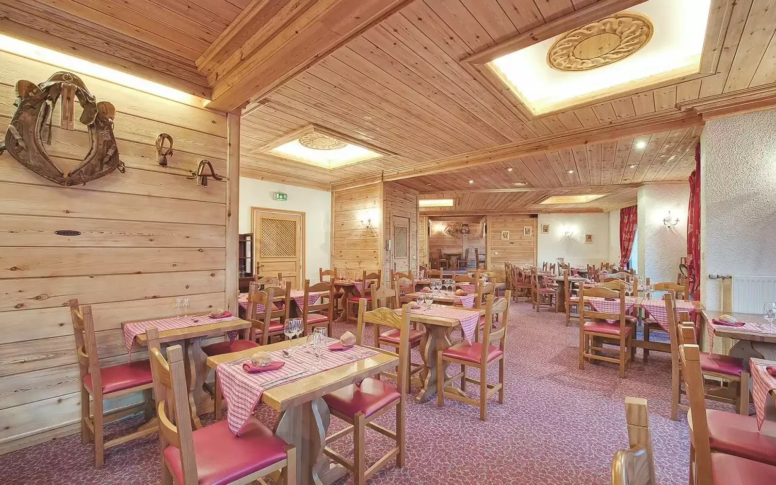 Restaurant with traditional wooden décor at the Meuire Chalet Hotel and Spa. Tables with checkered tablecloths and warm lighting create a welcoming atmosphere for meals.