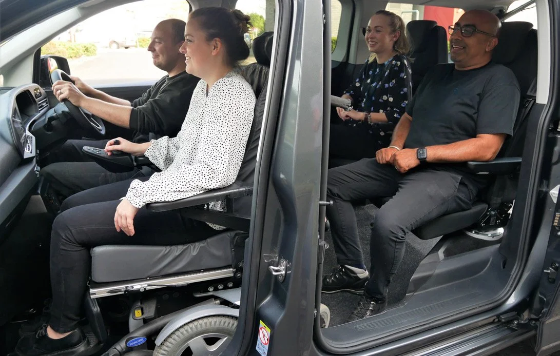 Wheelchair user riding up front beside the driver, with passengers in row two