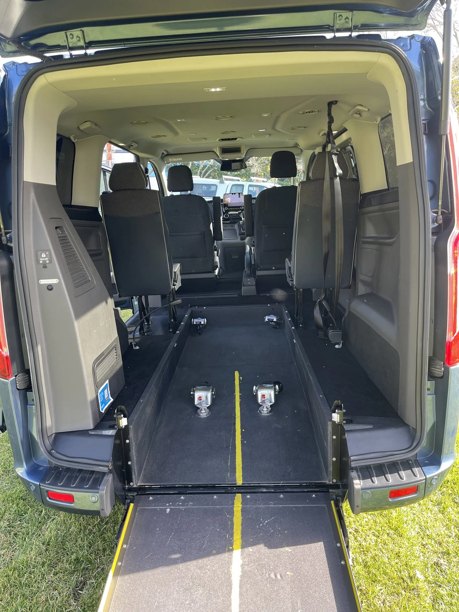 Ford Transit with rear doors open and ramp lowered, showing seating and wheelchair floor tracks