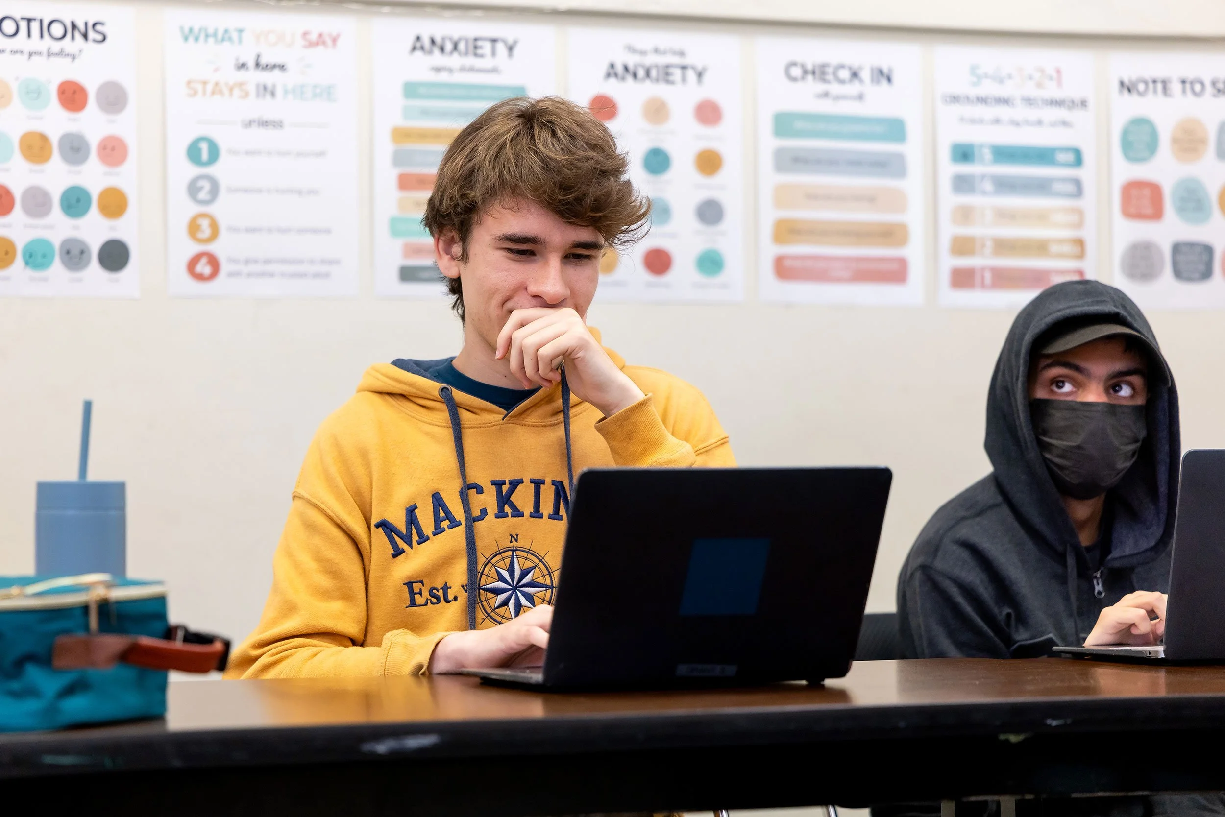 Student in yellow shirt works on laptop.