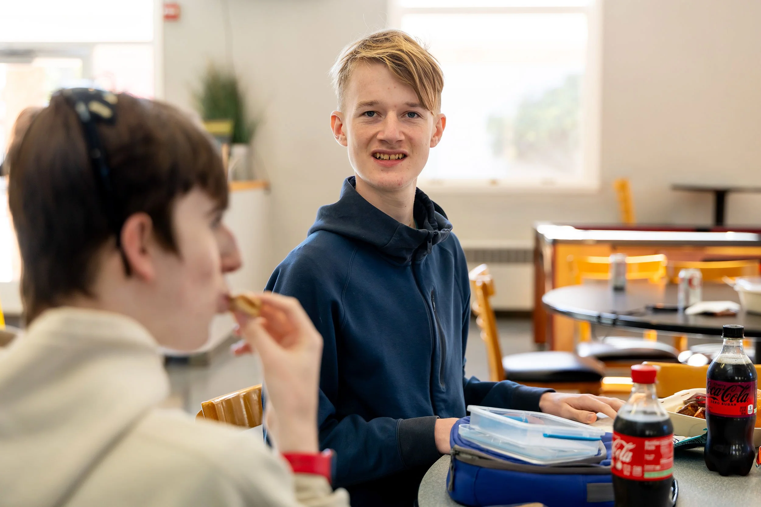 Two students at lunch, blonde students looks into camera smiling.