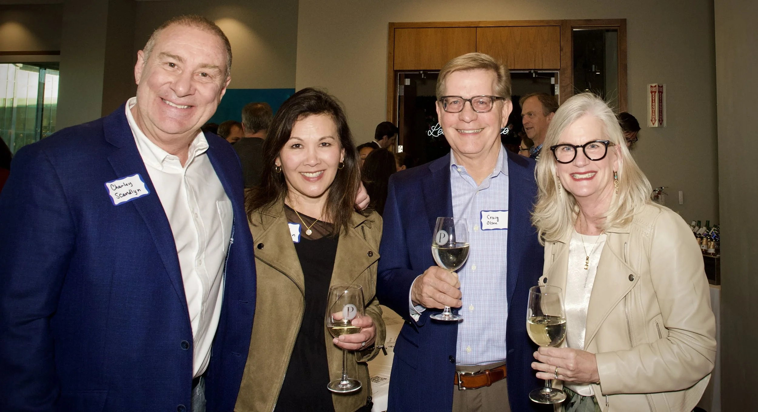 Four people at a social event smiling and holding wine glasses.