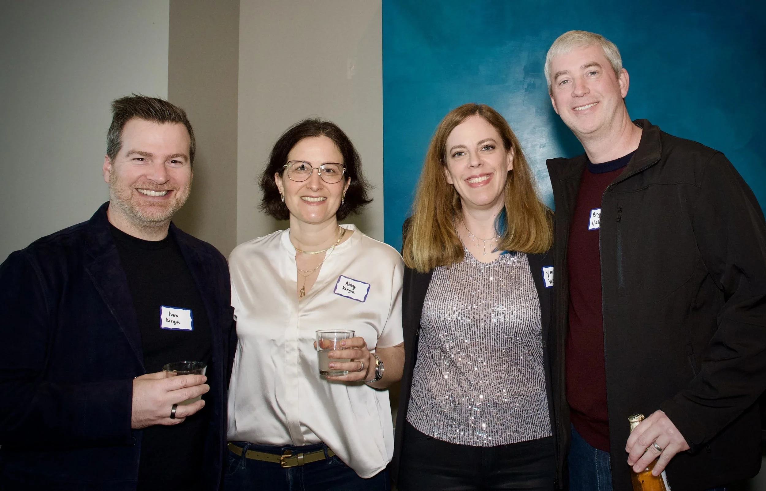 Four people standing together at a social event, smiling and holding drinks.