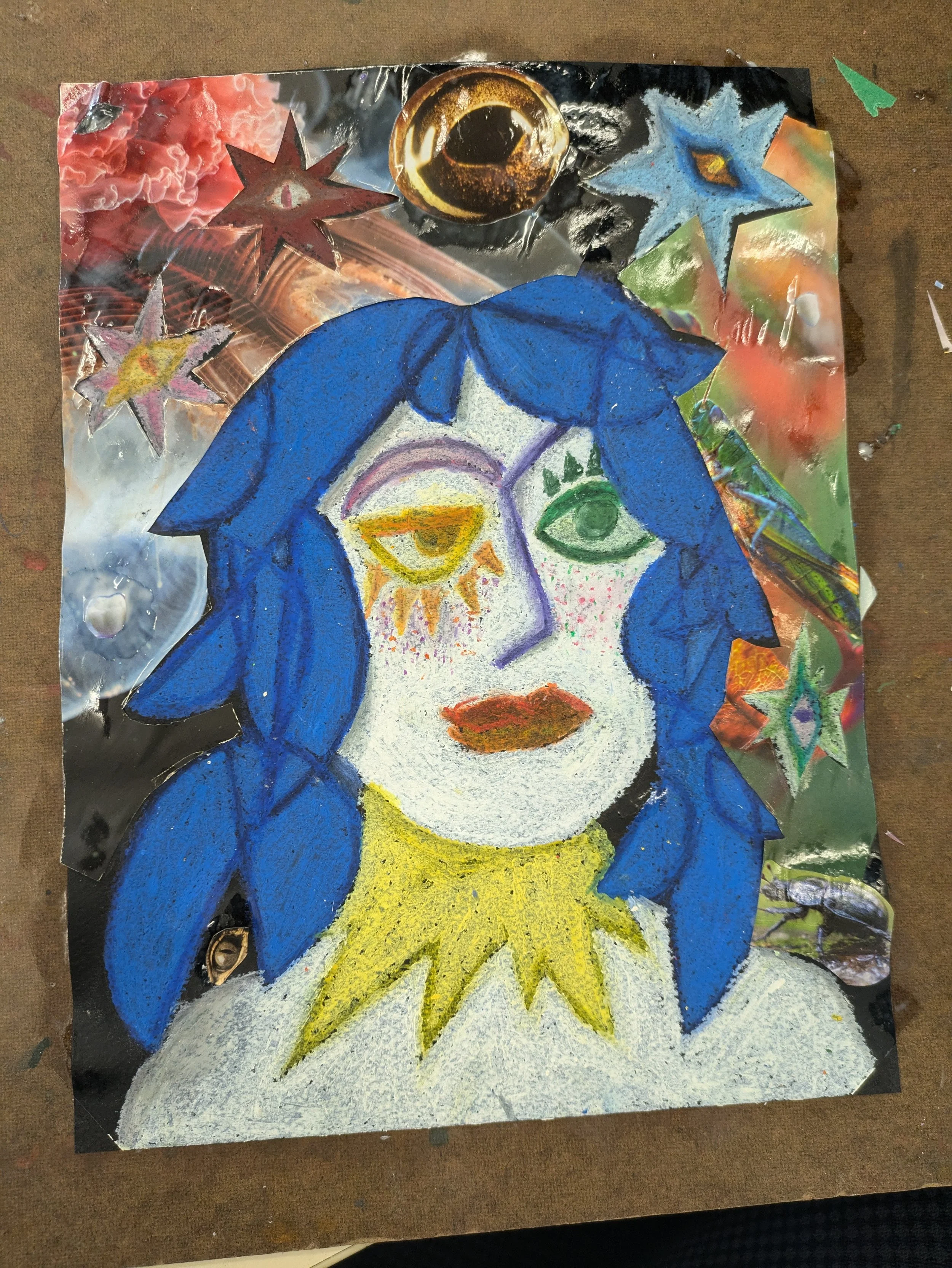 Mixed media artwork featuring a portrait of a person with blue hair and green eyes, surrounded by colorful stars and abstract elements, created with paint and collage on reflective foil.