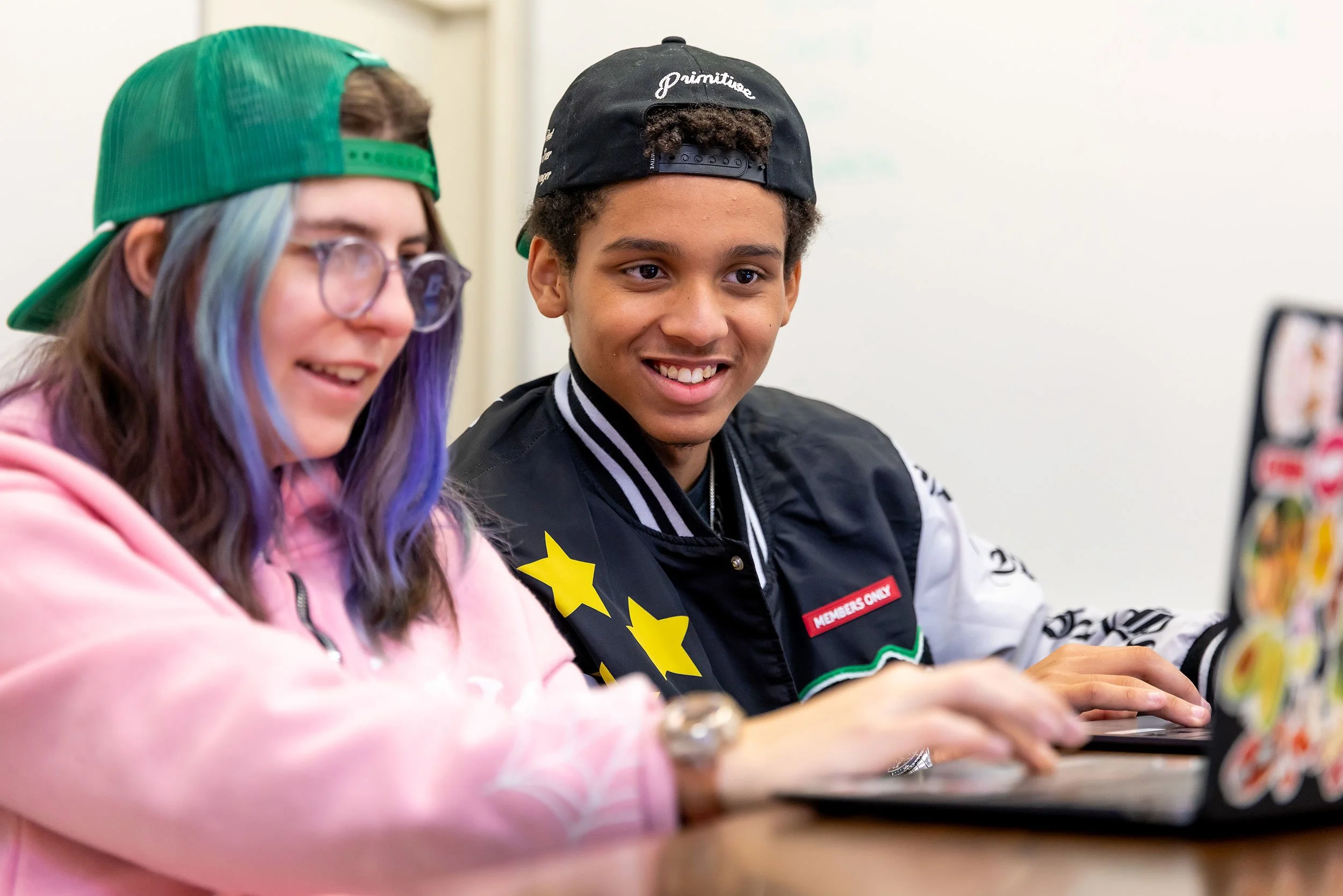 Two smiling students work on laptop in classroom