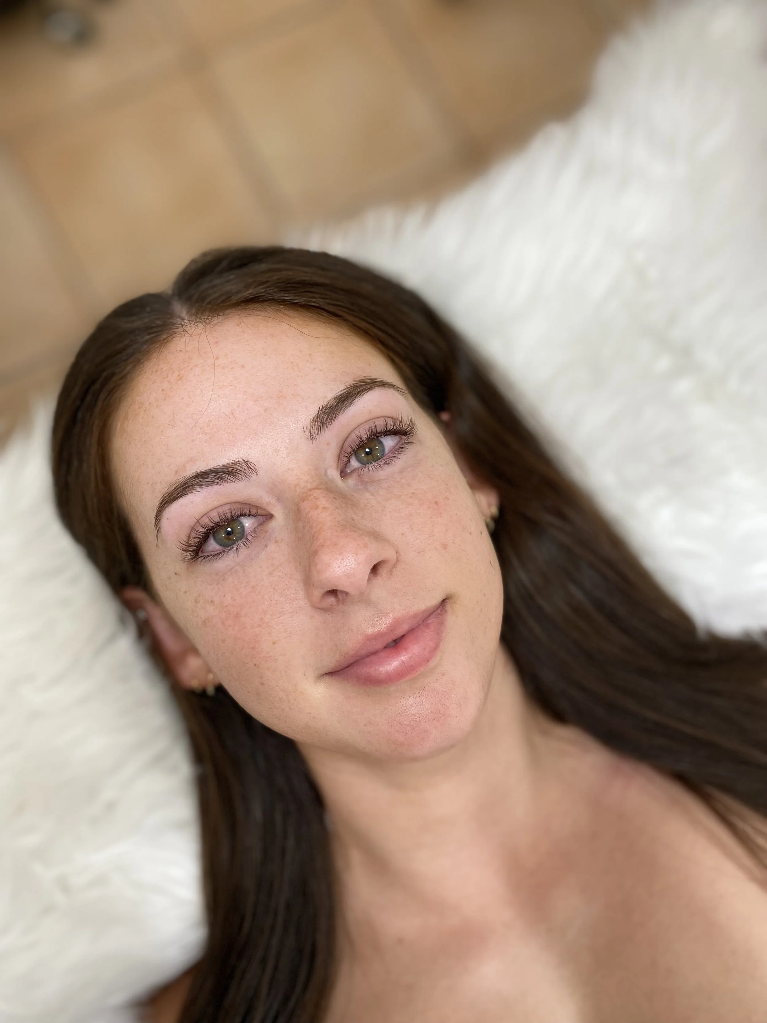 Close-up of a young woman's face with brown hair, fair skin, freckles, and green eyes, brown lash extensions to enhance natural lashes.