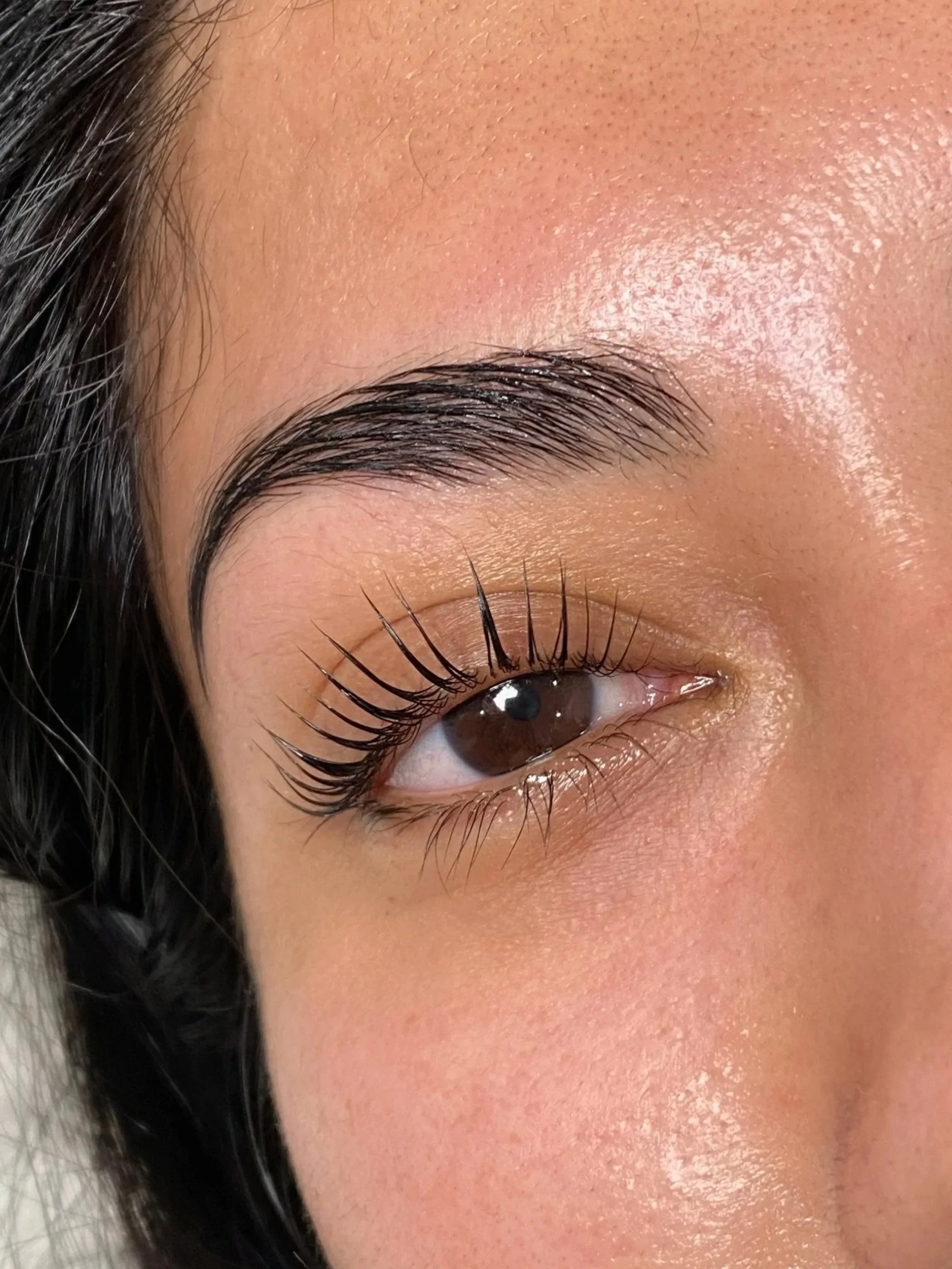 Close-up of a person's closed eye, showing well-groomed eyebrow, long eyelashes, and smooth skin with a natural glow.
