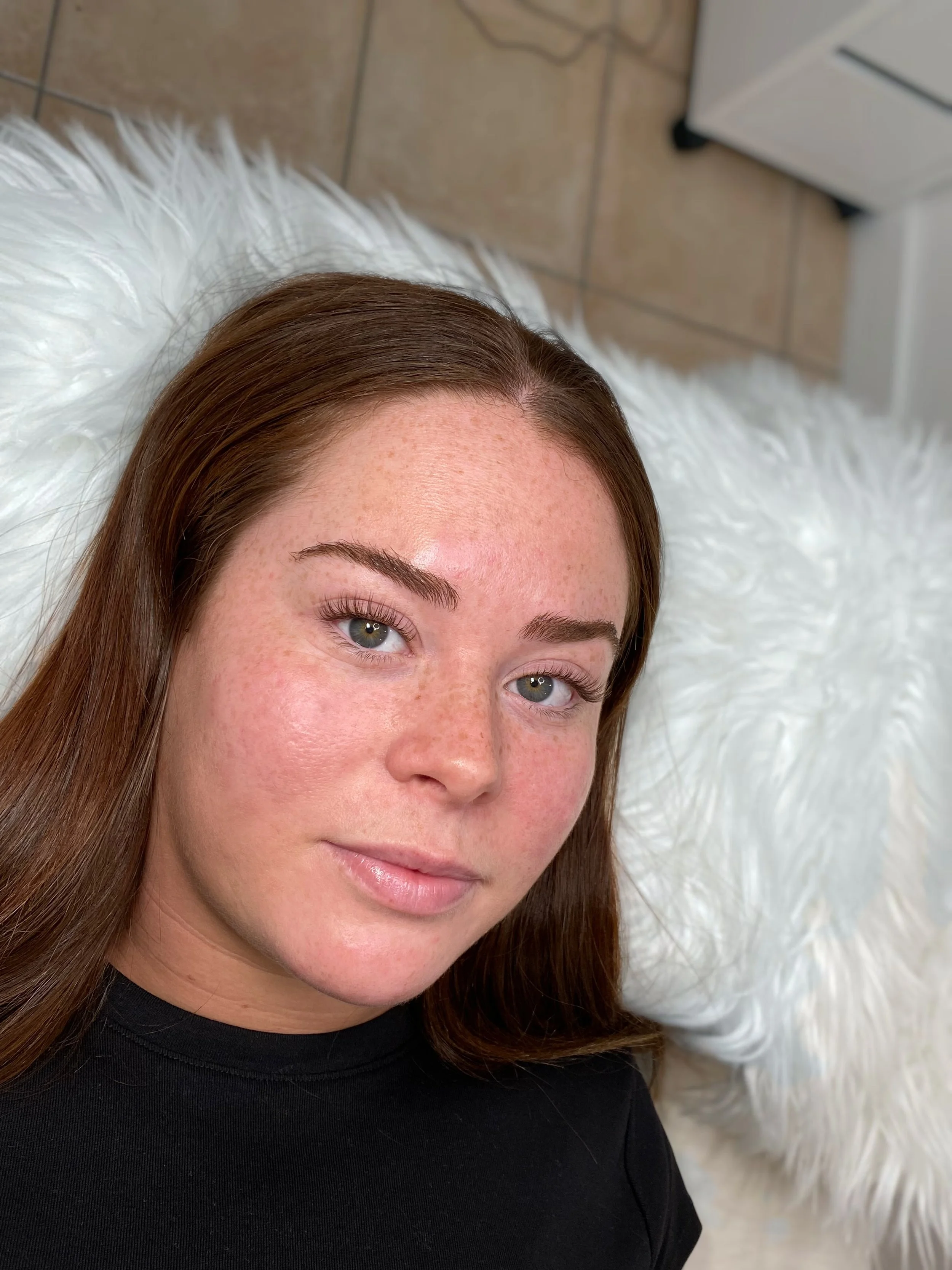 Close-up of a woman with long brown hair, fair skin with freckles, and green eyes. Brown natural looking lash extensions to enhance natural features