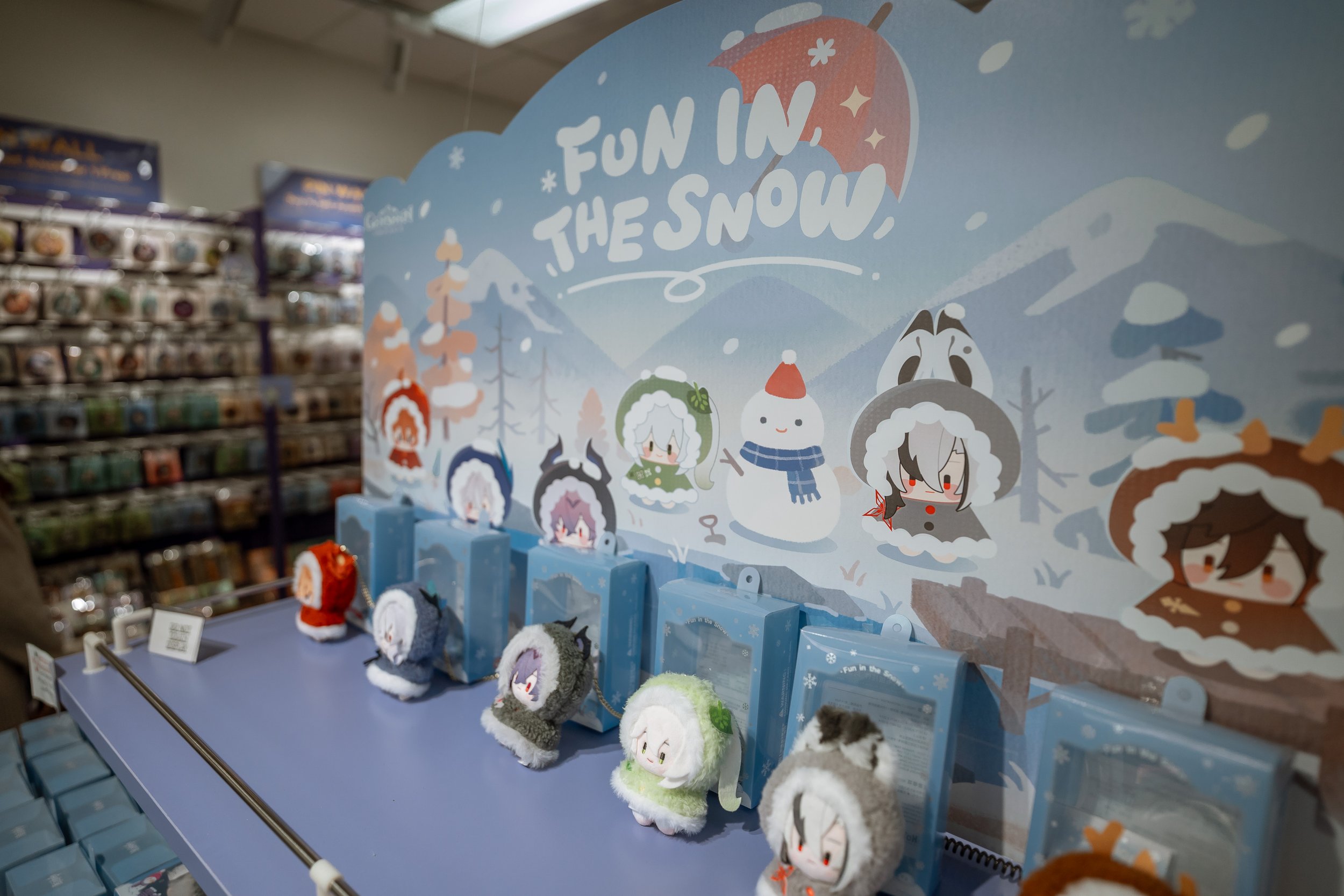 Display of plush snowman and animal toys with a winter and snow theme, featuring a background with snow-covered trees and the phrase 'Fun in the Snow'.