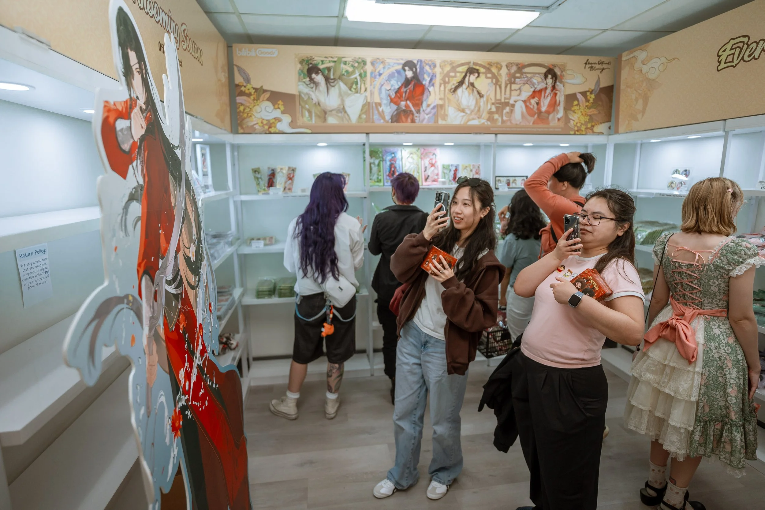Group of people at an indoor event, looking at artwork or displays on the walls, some taking photos with their phones.