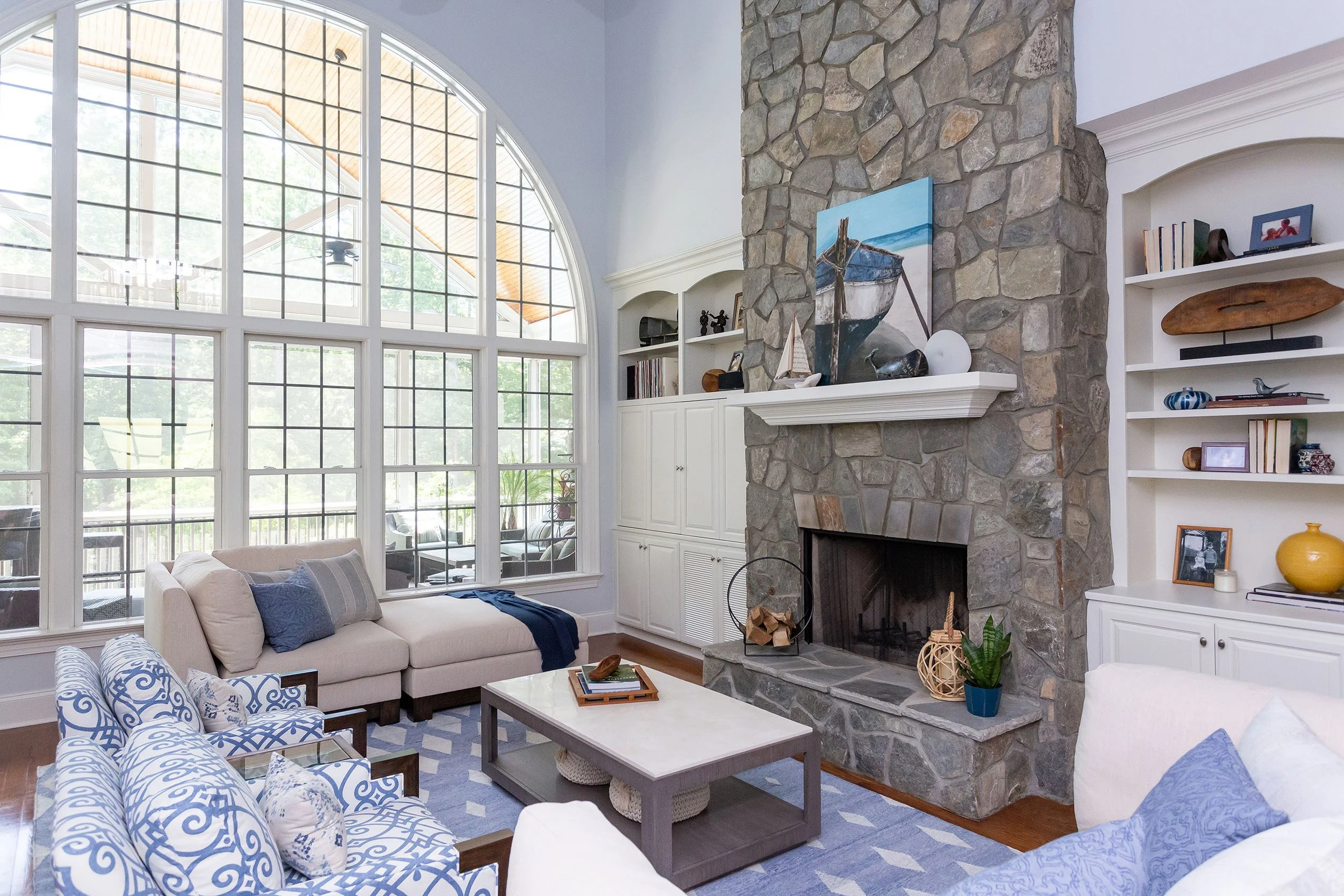 two story living room design in contemporary coastal home design with blue walls stone fireplace custom upholstered chairs and chaise lounge in durham north carolina by cat french design durham interior designer