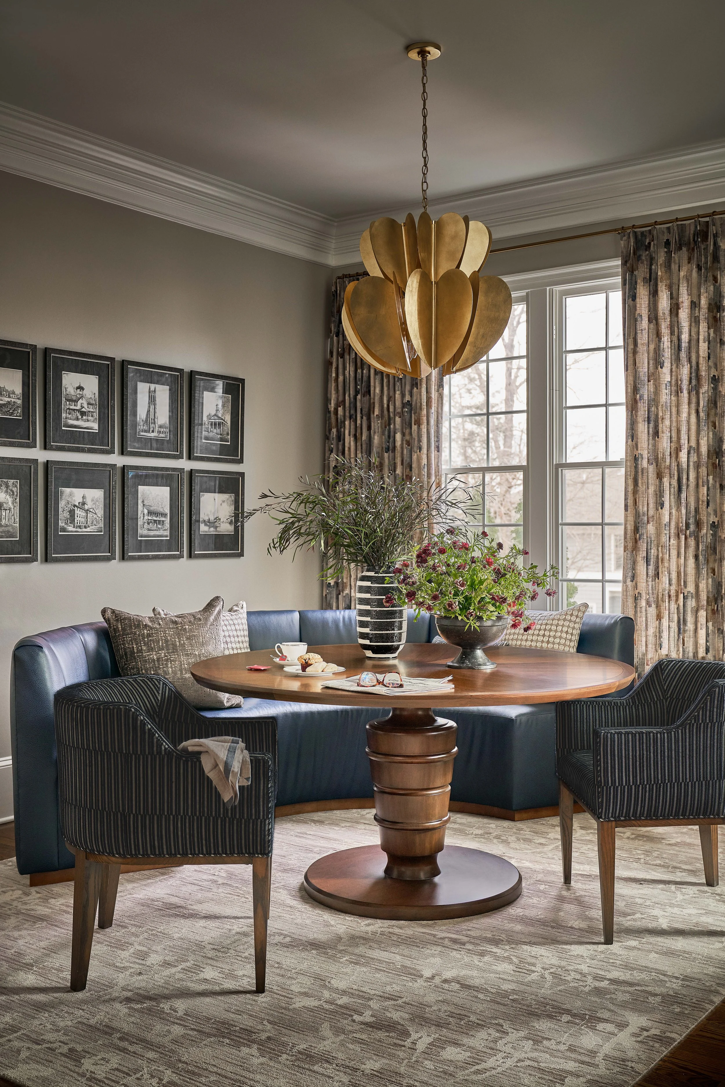 dining room with round pedestal table and curved blue banquette with gold art deco chandelier and black and white art prints on the wall designed by cat french design chapel hill interior designer durham interior designer luxury townhome design