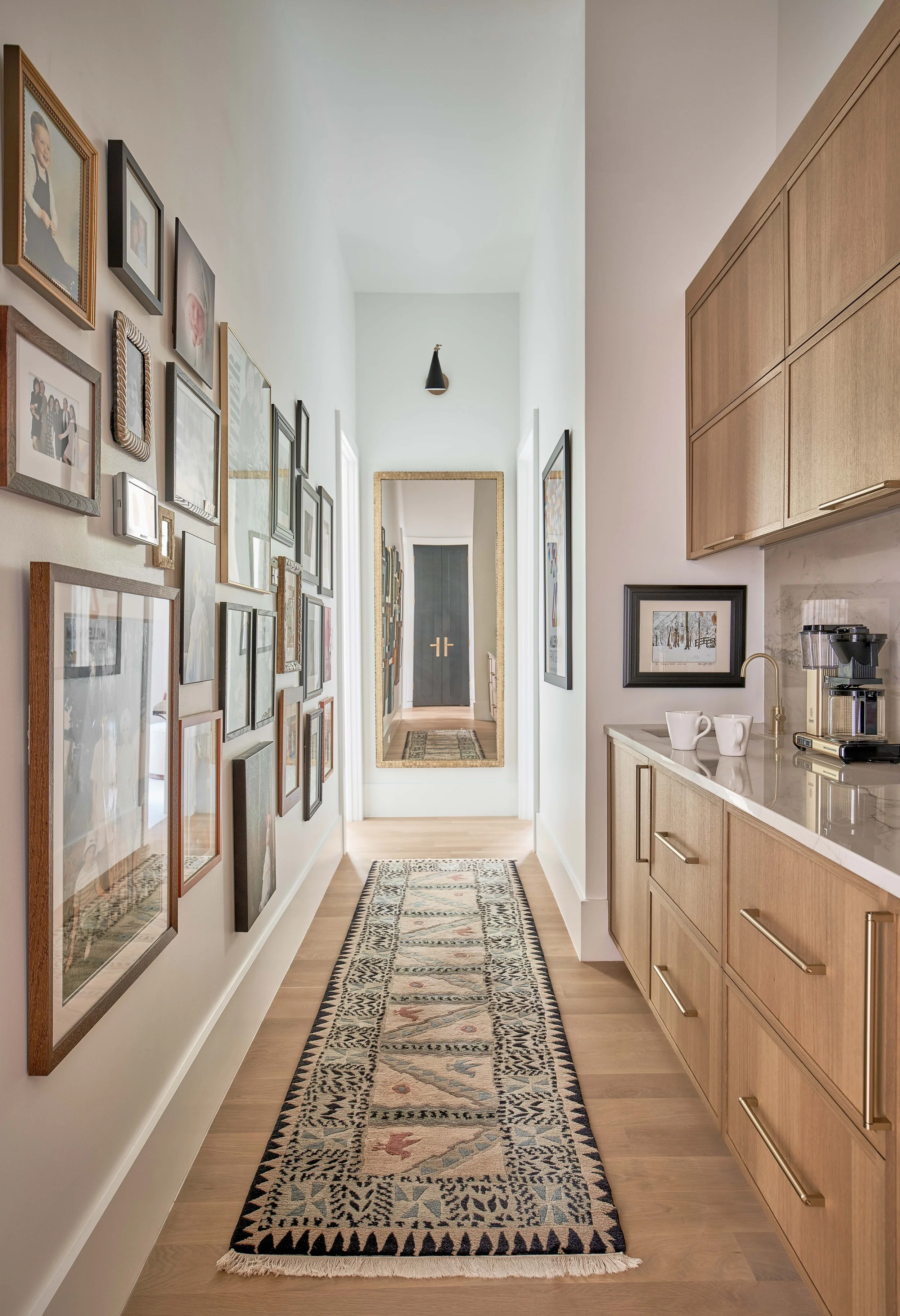 view of a hallway with a custom gallery wall and a wet bar coffee bar station with custom cabinetry in a primary bedroom and dual primary bathroom design by cat french design in a durham custom home interior design luxury interior designer nc