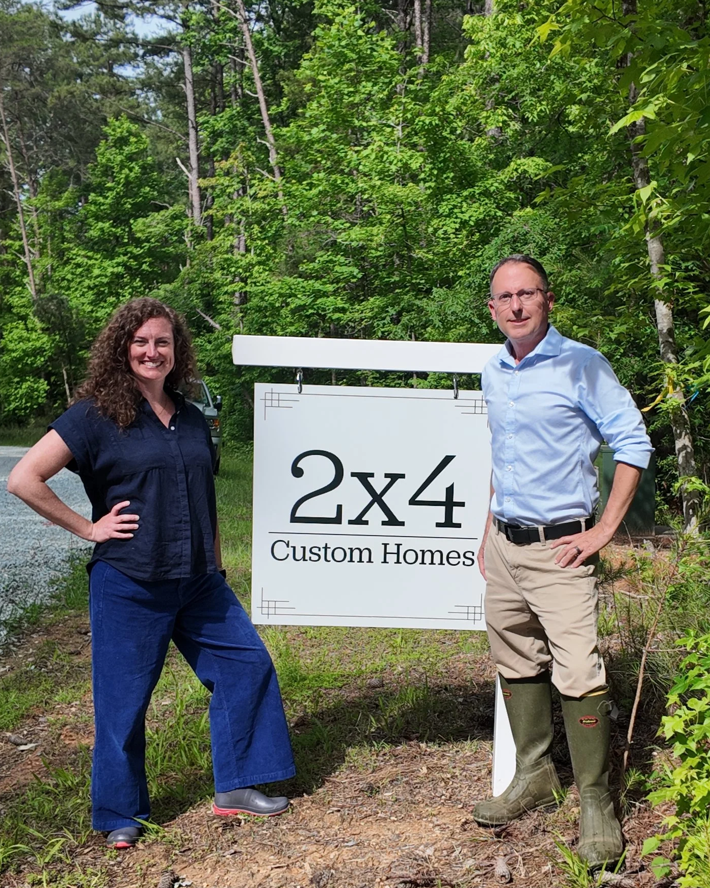 Cat French and Chad Collins stand by a white sign showing 2x4 custom homes at groundbreaking for custom home design chapel hill interior designer